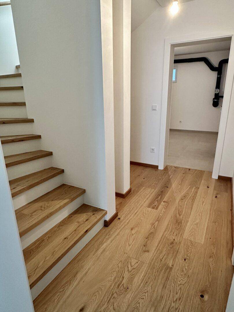 Heller Flur mit Holztreppe und Eichenparkett, der zu einem weiteren Raum führt.