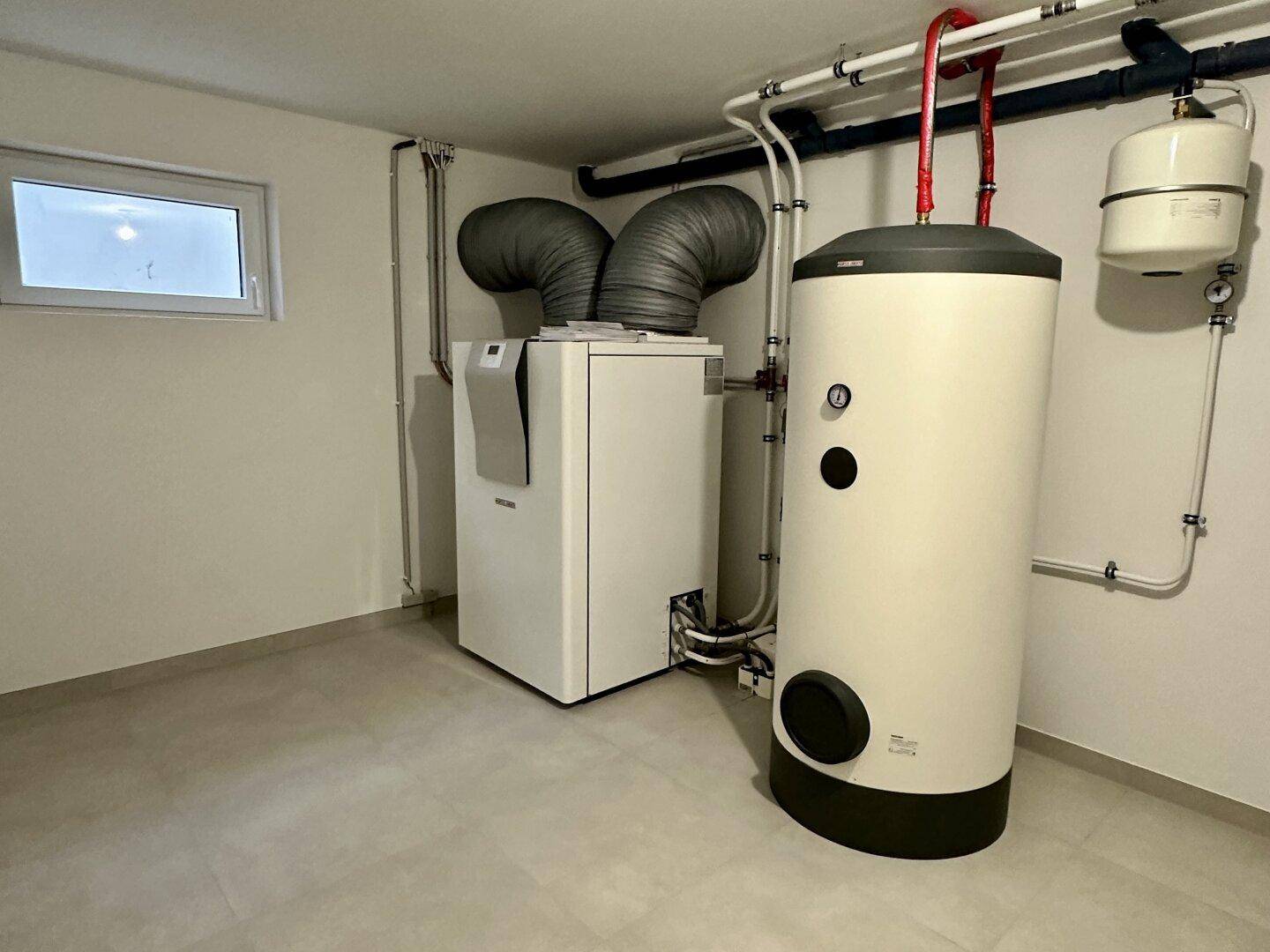 Technikraum im Keller mit moderner Heizungsanlage, Warmwasserspeicher und sichtbaren Leitungen.