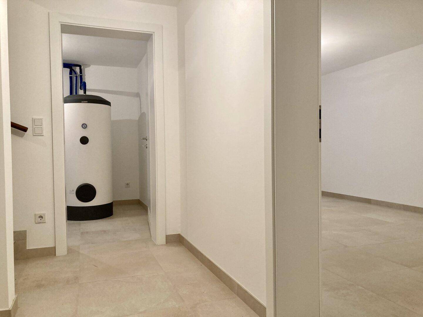 Hauswirtschaftsraum mit Fliesenboden und großem Warmwasserspeicher für die Warmwasserversorgung.