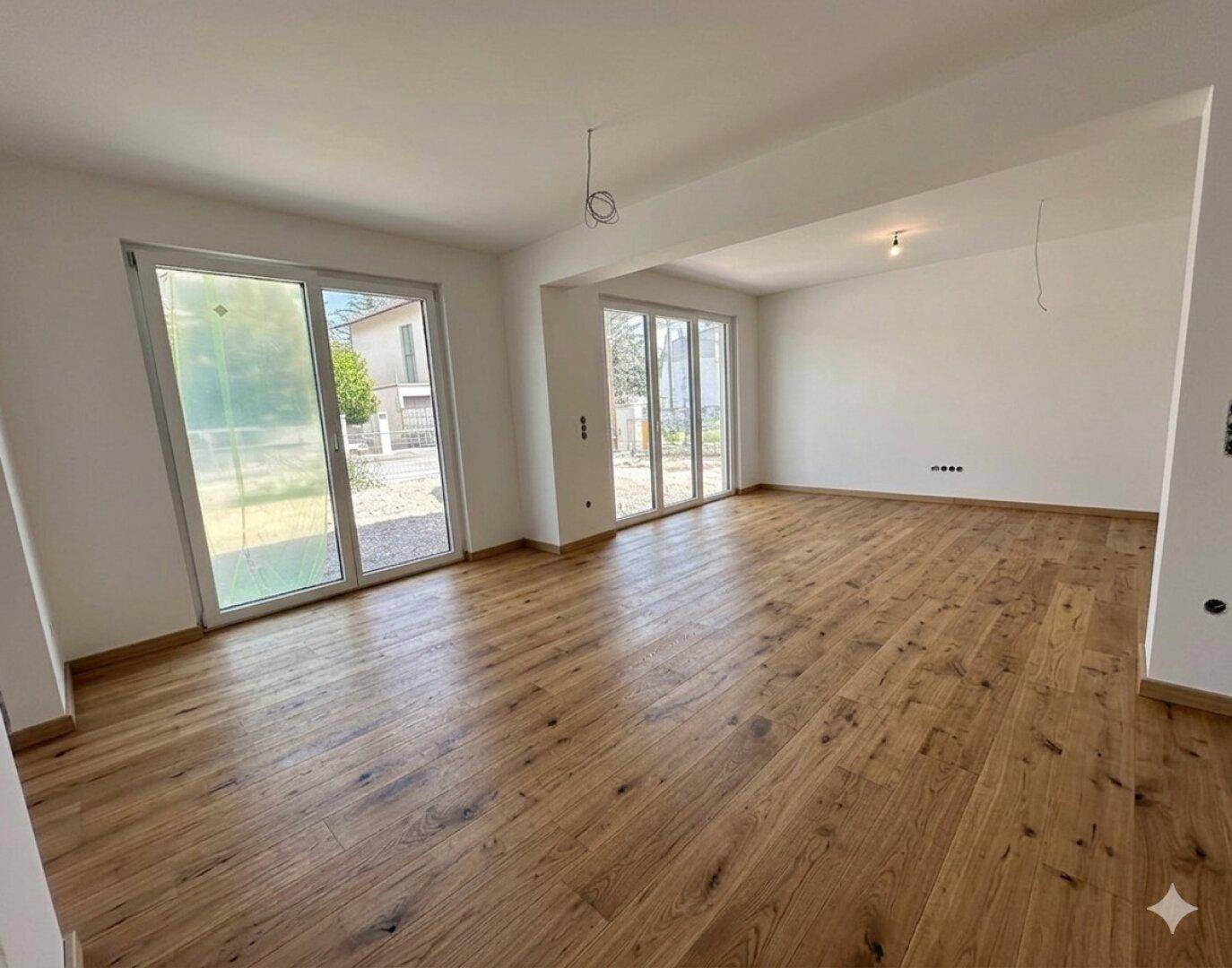 Geräumiges, helles Wohnzimmer mit großen Fenstern und hochwertigem Parkettboden, bereit für die Einrichtung.
