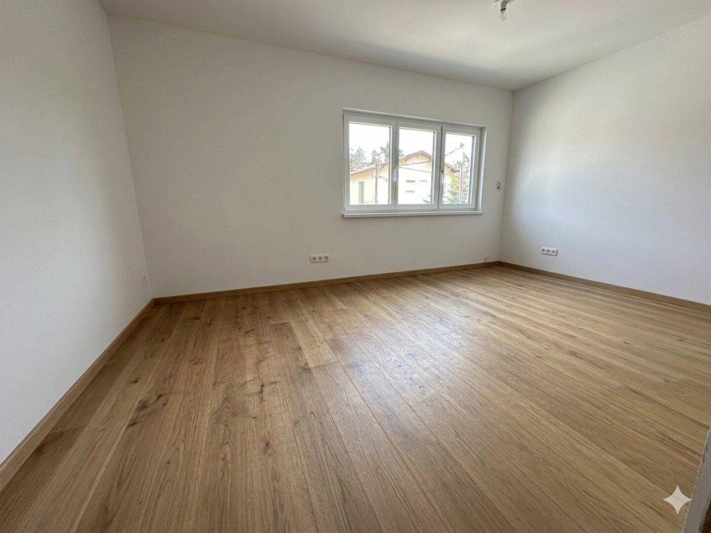 Freundliches Schlafzimmer mit großen Fenstern und elegantem Holzboden, ideal für eine ruhige Rückzugsmöglichkeit.