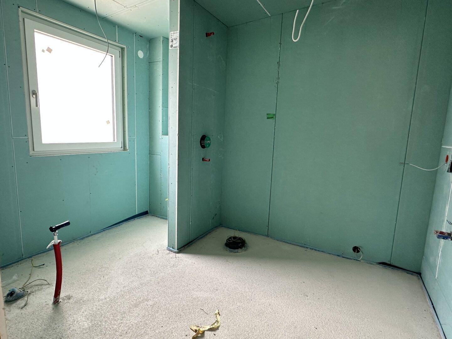 Badezimmer im Rohbau mit Fenster, bereit für die Installation moderner Sanitäreinrichtungen.