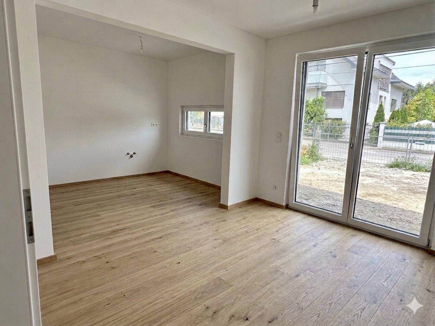 Heller Wohnbereich mit großen Fenstern und Holzboden, ideal für offenes Wohnen und viel Tageslicht.
