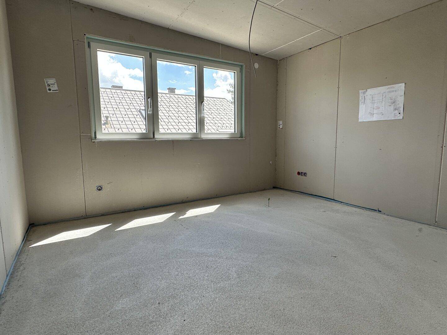 Schlafzimmer im Rohbau mit Fenster und Dachschräge, bietet Potenzial für individuelle Gestaltung.