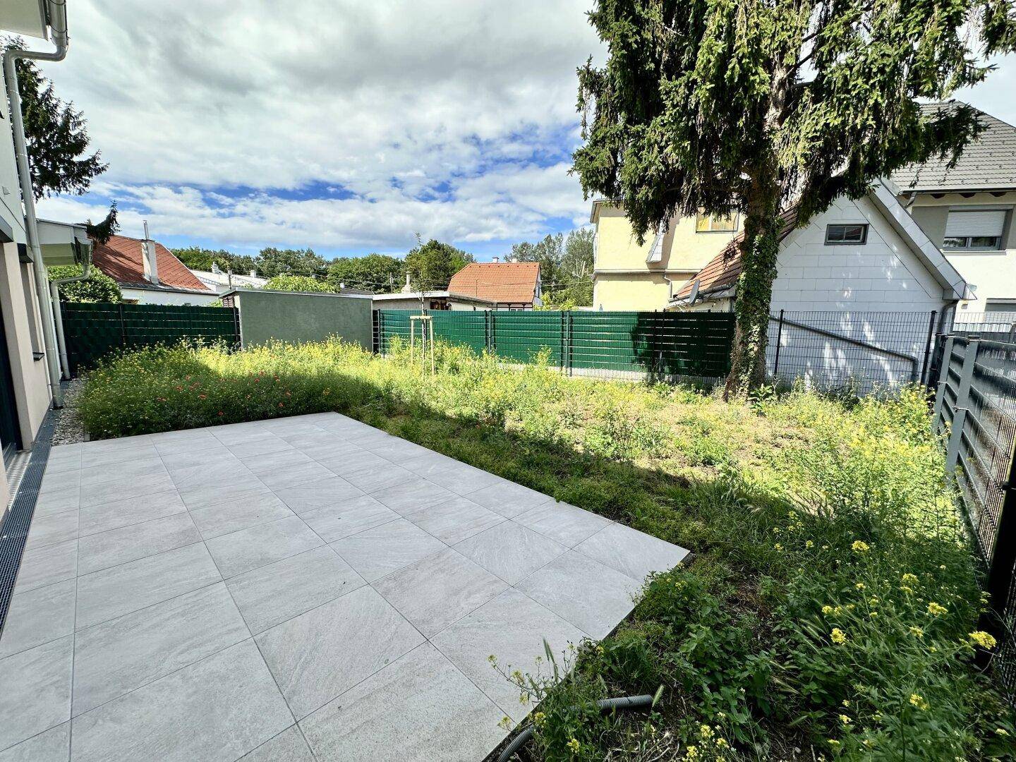 Gepflasterte Terrasse mit angrenzendem Gartenbereich, der noch gestaltet werden muss.
