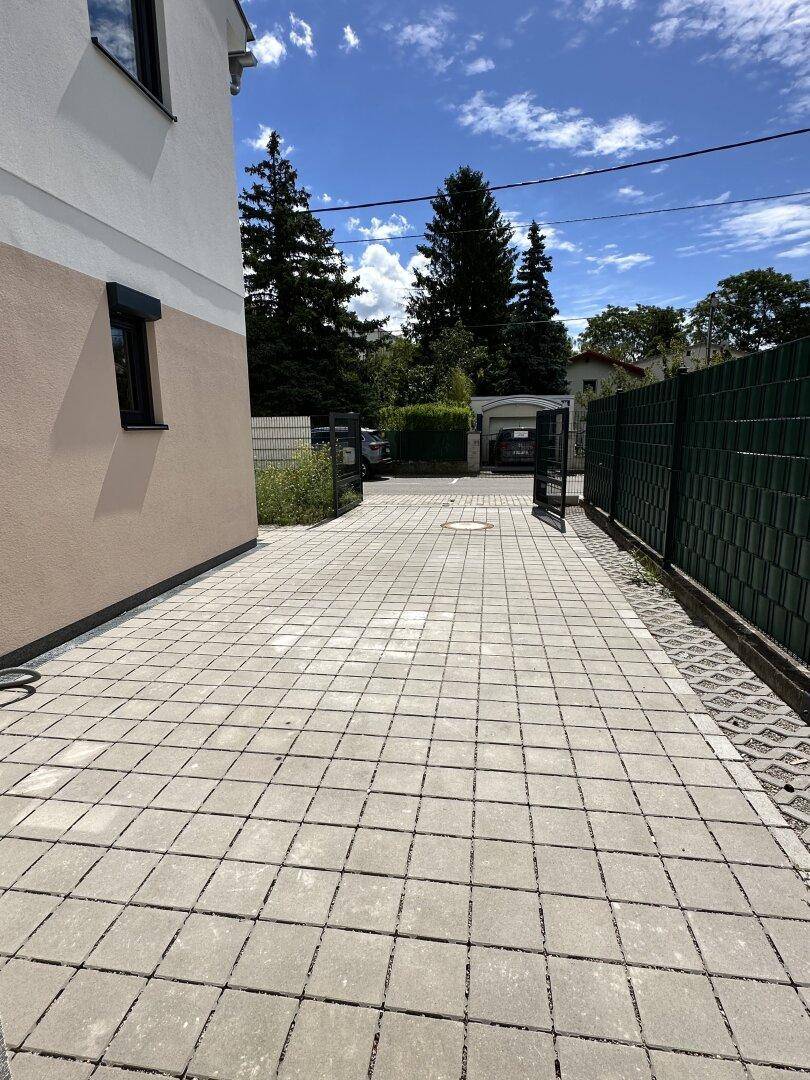 Gepflasterte Einfahrt zum Haus mit seitlichem Zaun und Zugang zum Grundstück.