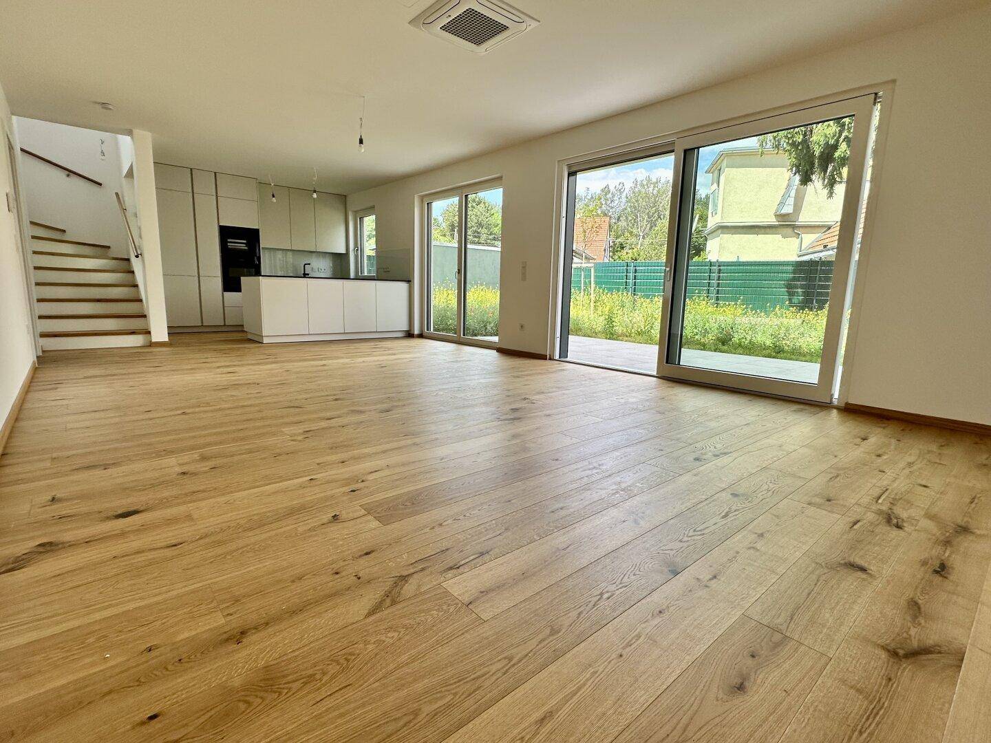 Heller offener Wohnbereich mit Holzboden, moderner Küche und großen Schiebetüren zum Garten.