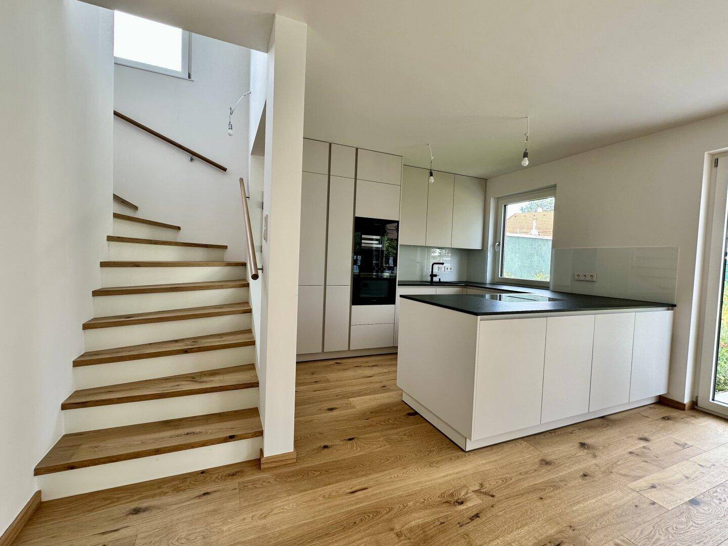Offener Wohnbereich mit moderner Küche und eleganter Holztreppe, die die Etagen verbindet.