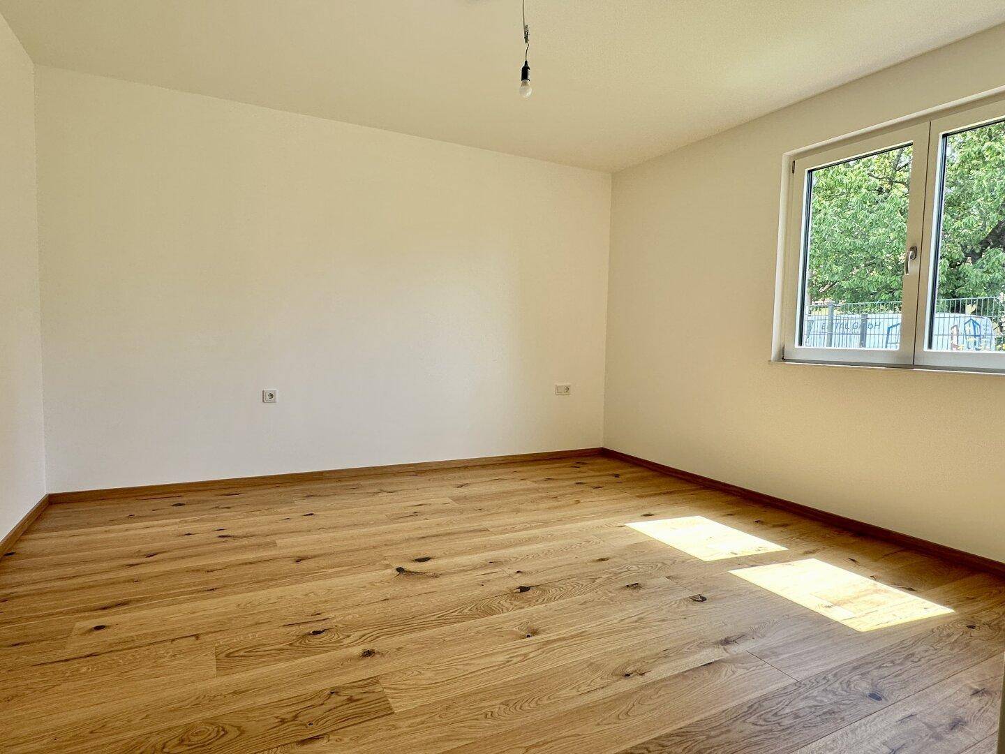 Sonniges Schlafzimmer mit Holzboden und großem Fenster, das den Raum mit Licht erfüllt.