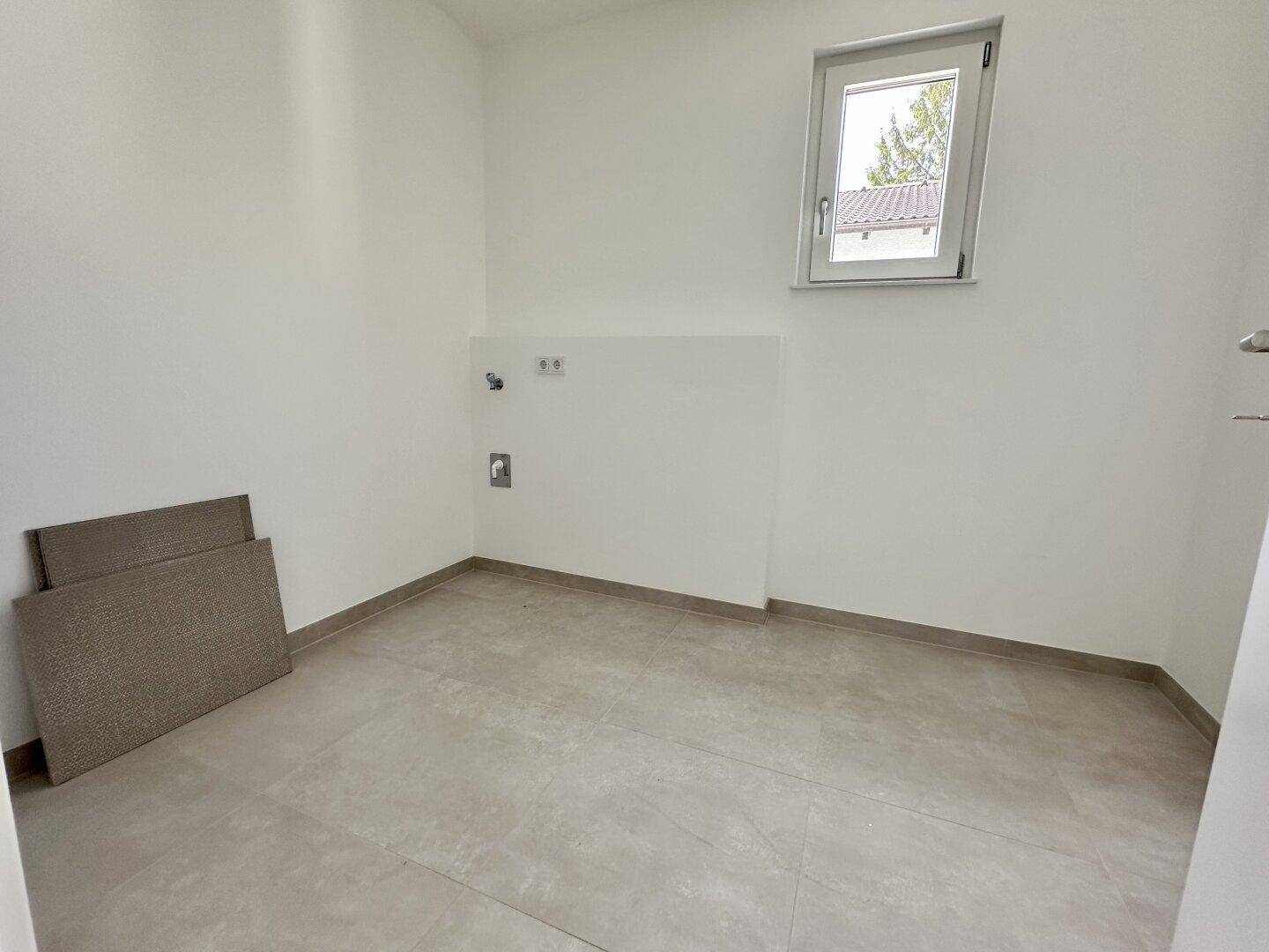 Praktischer Hauswirtschaftsraum mit Fliesenboden und Fenster, ideal für Waschmaschine und Trockner.