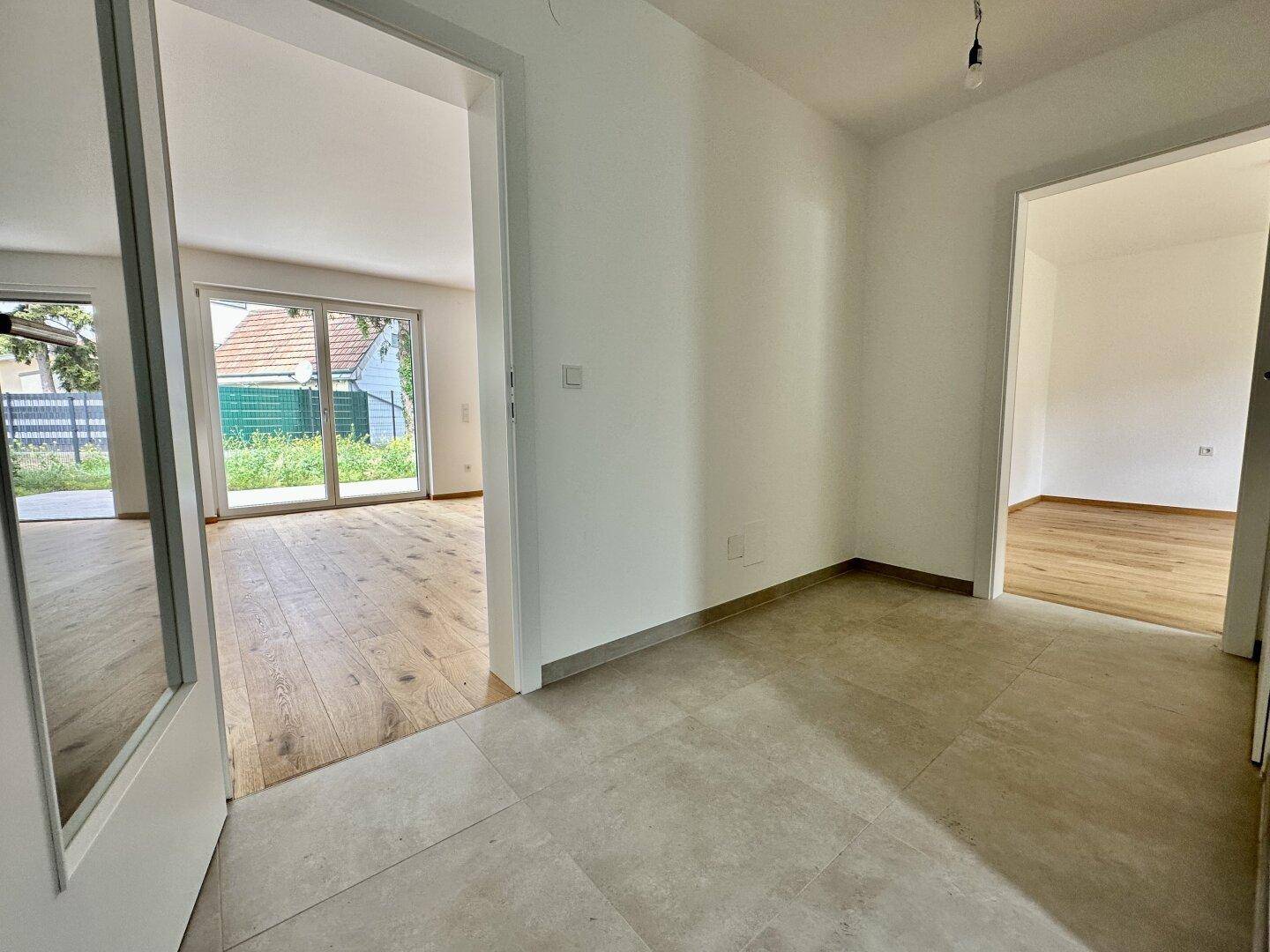 Eingangsbereich mit Fliesenboden, der zu den angrenzenden Zimmern mit Holzboden führt.