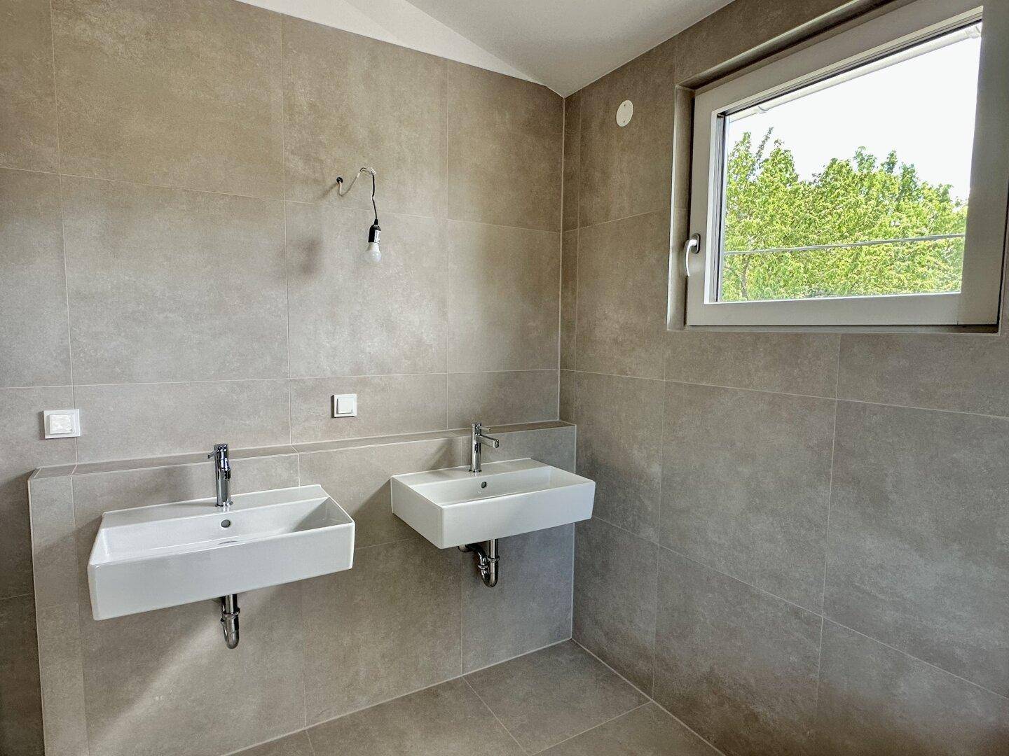 Helles Badezimmer mit zwei modernen Waschbecken und einem Fenster für natürliche Belüftung.