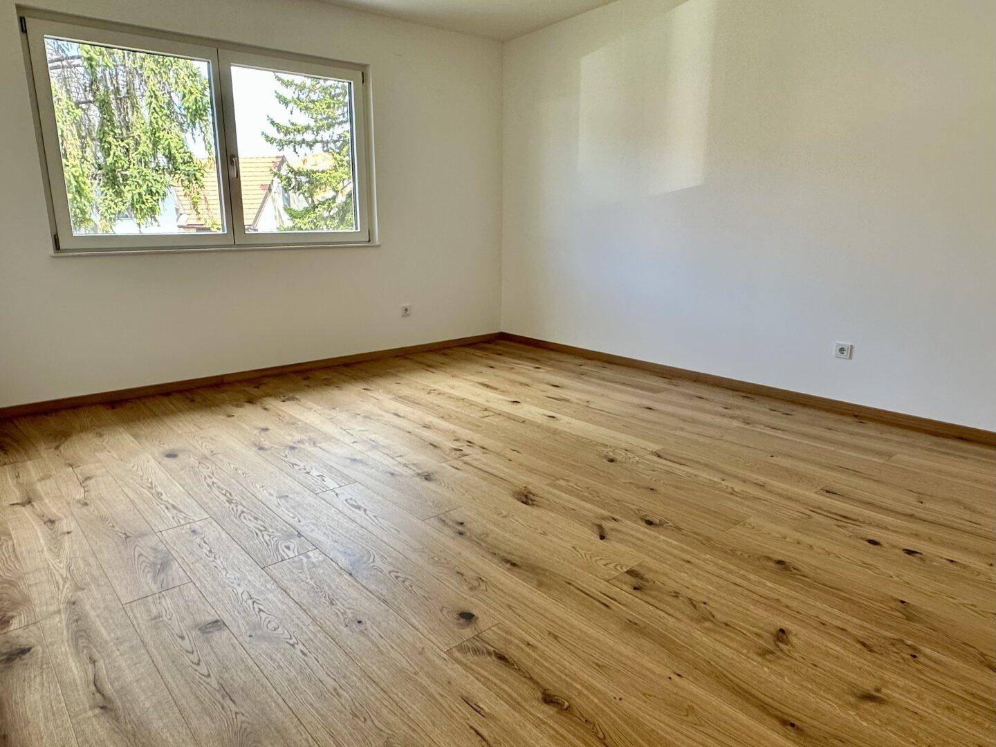 Helles Schlafzimmer mit Holzboden und Fenster, das eine angenehme Atmosphäre schafft.