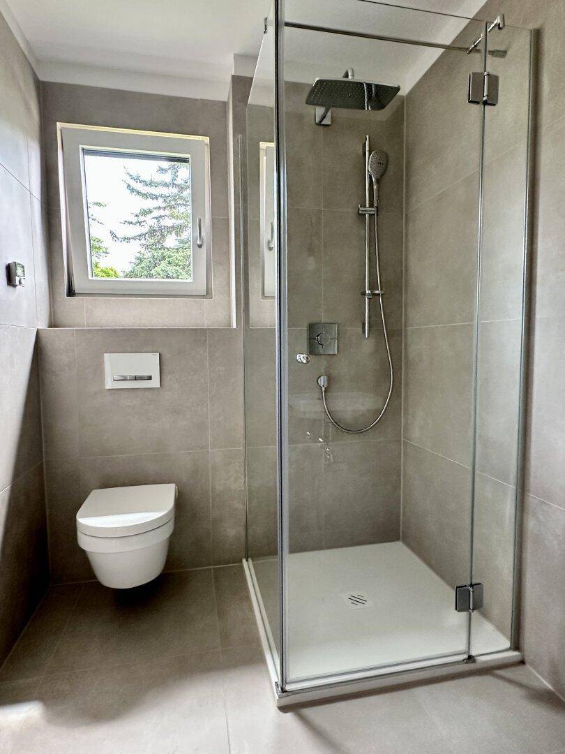 Modernes Badezimmer mit begehbarer Dusche, wandhängendem WC und Fenster für Tageslicht.