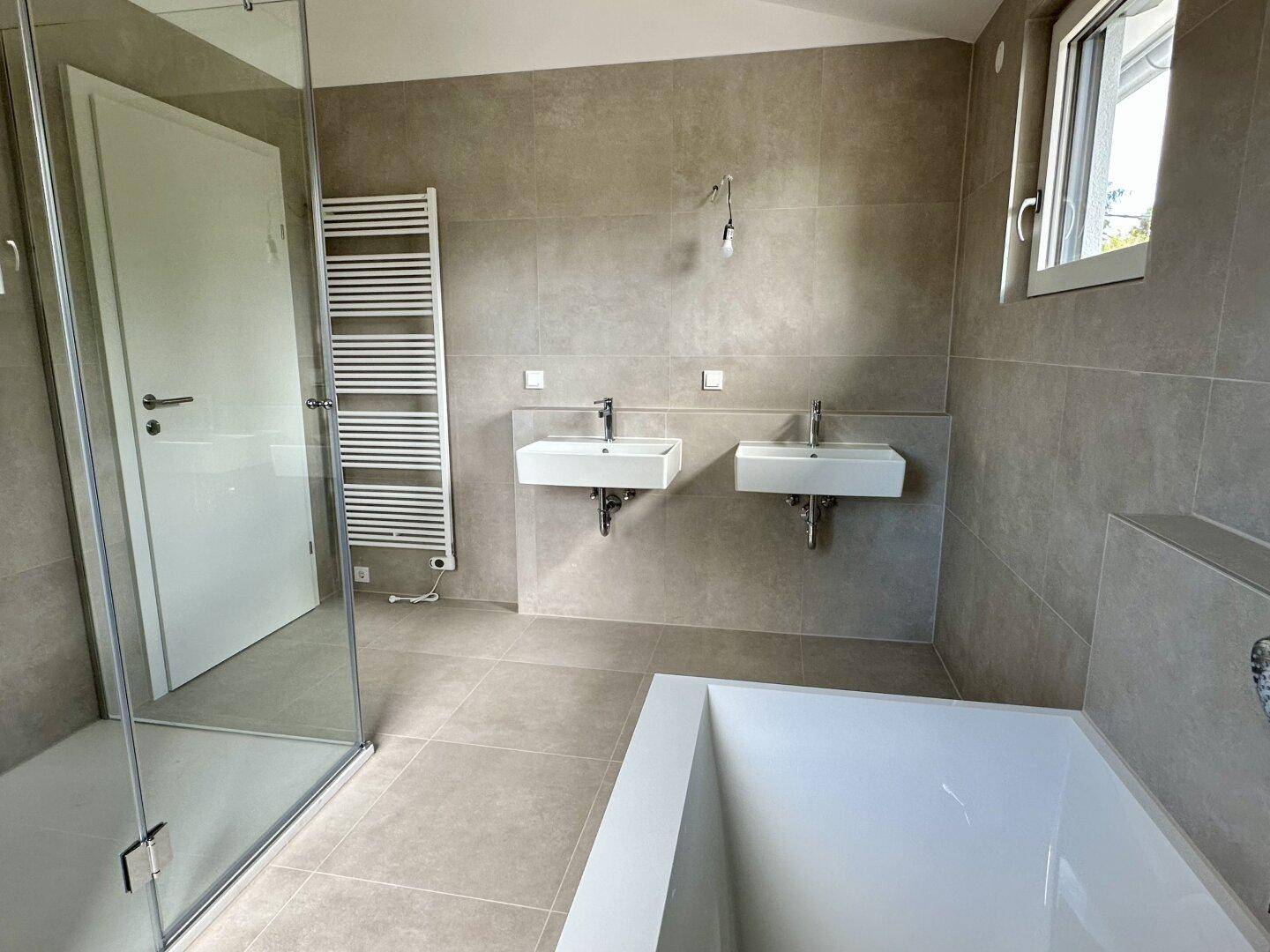 Modernes Badezimmer mit zwei Waschbecken, Badewanne, begehbarer Dusche und Handtuchheizkörper.
