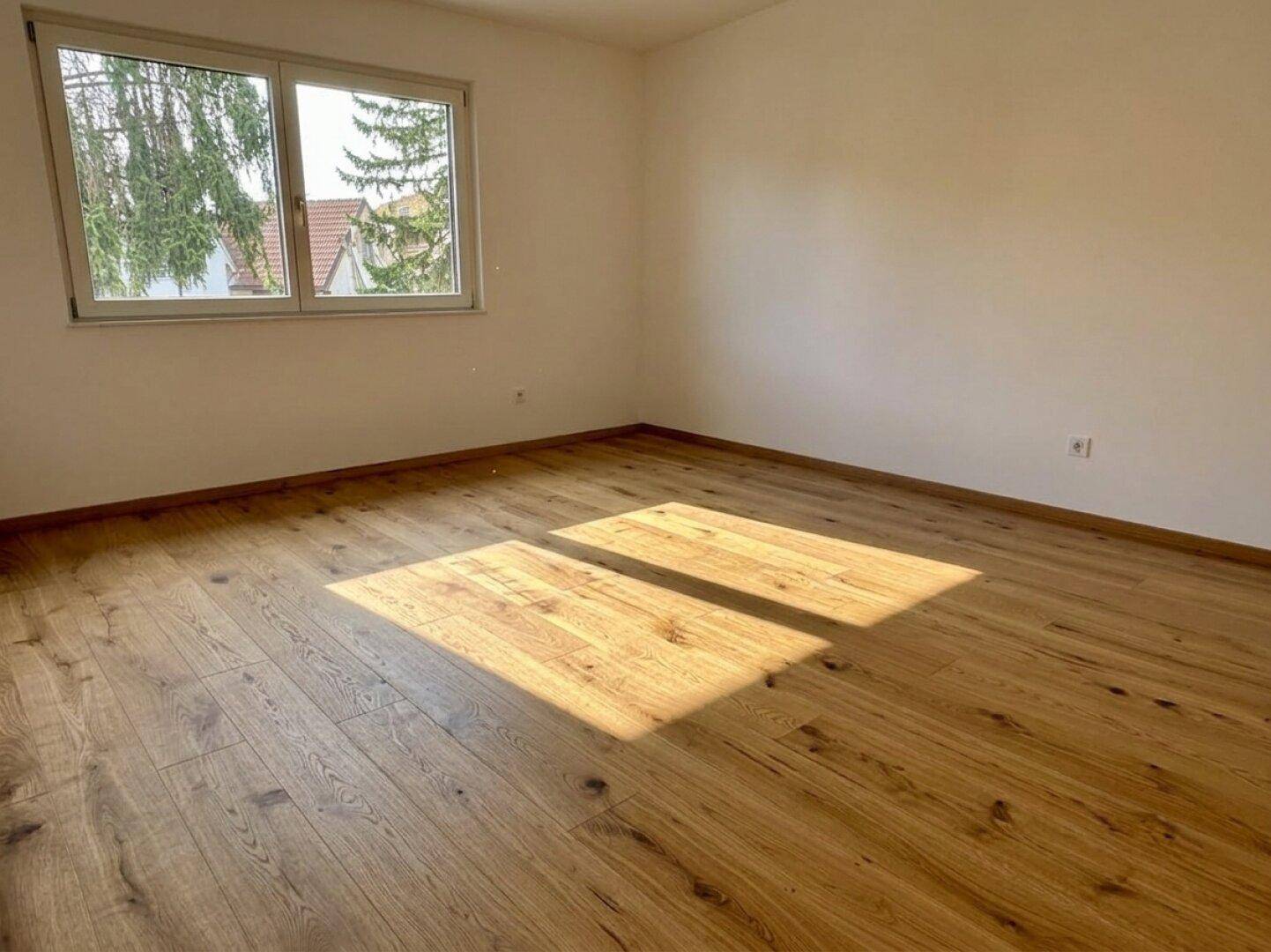 Helles Schlafzimmer mit Eichenparkettboden und großem Fenster mit Blick ins Grüne.