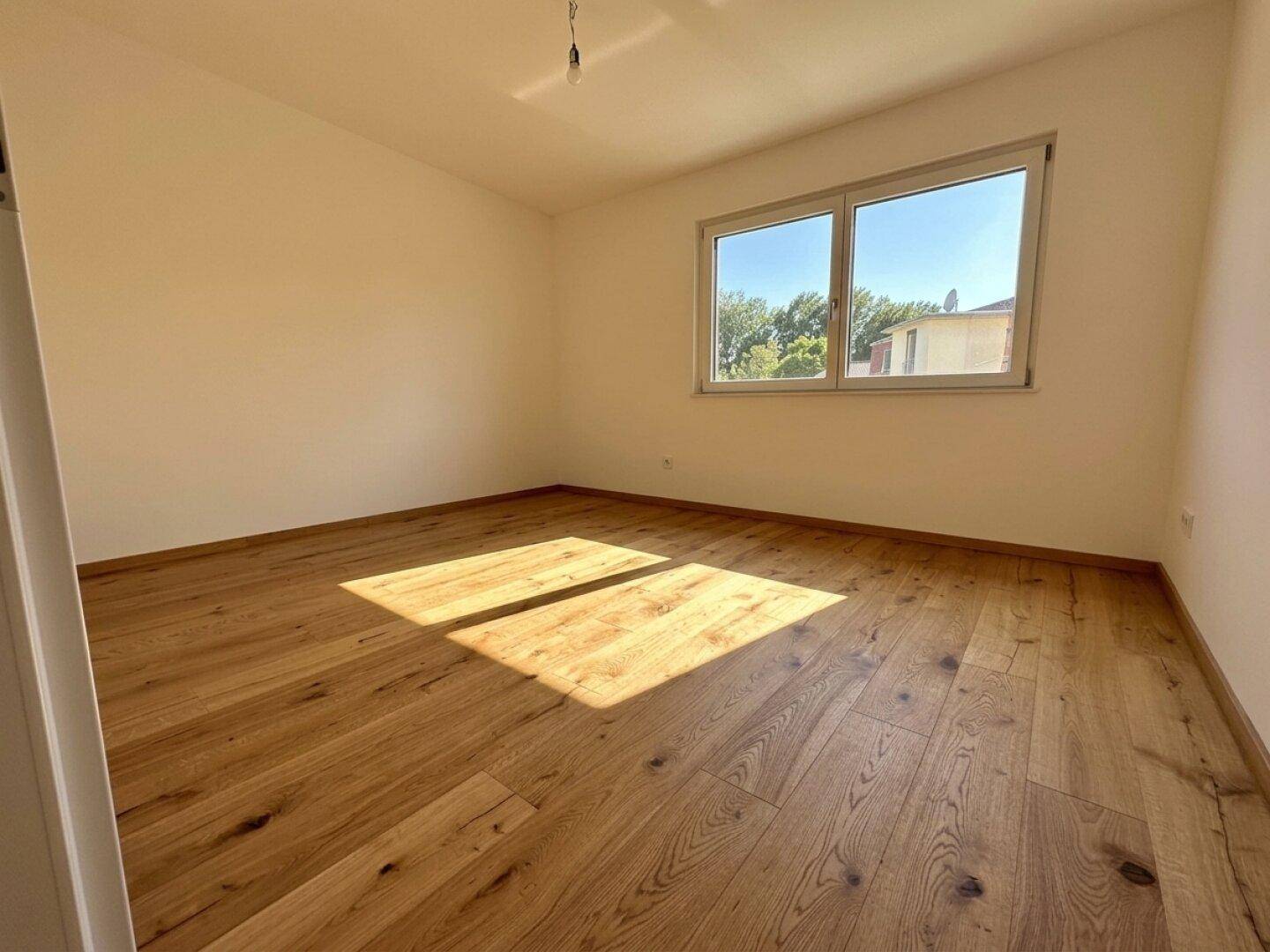 Sonniger Raum mit hellem Holzboden und Fenster, das viel Tageslicht hereinlässt.