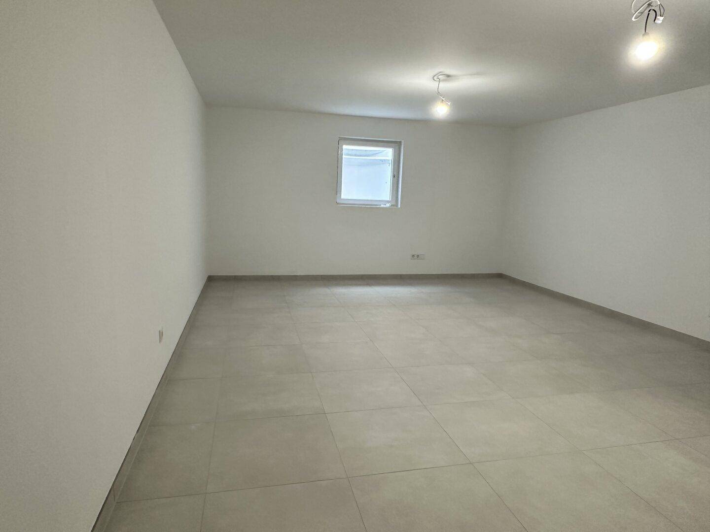 Heller Raum mit modernen Fliesen, weißen Wänden und einem Fenster, ideal für Wohn- oder Schlafzimmer.