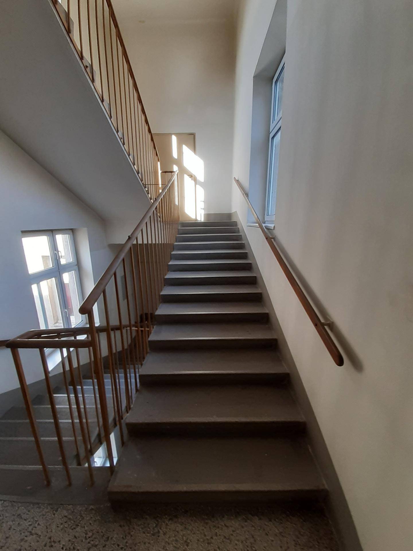 Geräumiger Treppenbereich mit viel Tageslicht, robusten Stufen und einem einfachen Holzhandlauf.