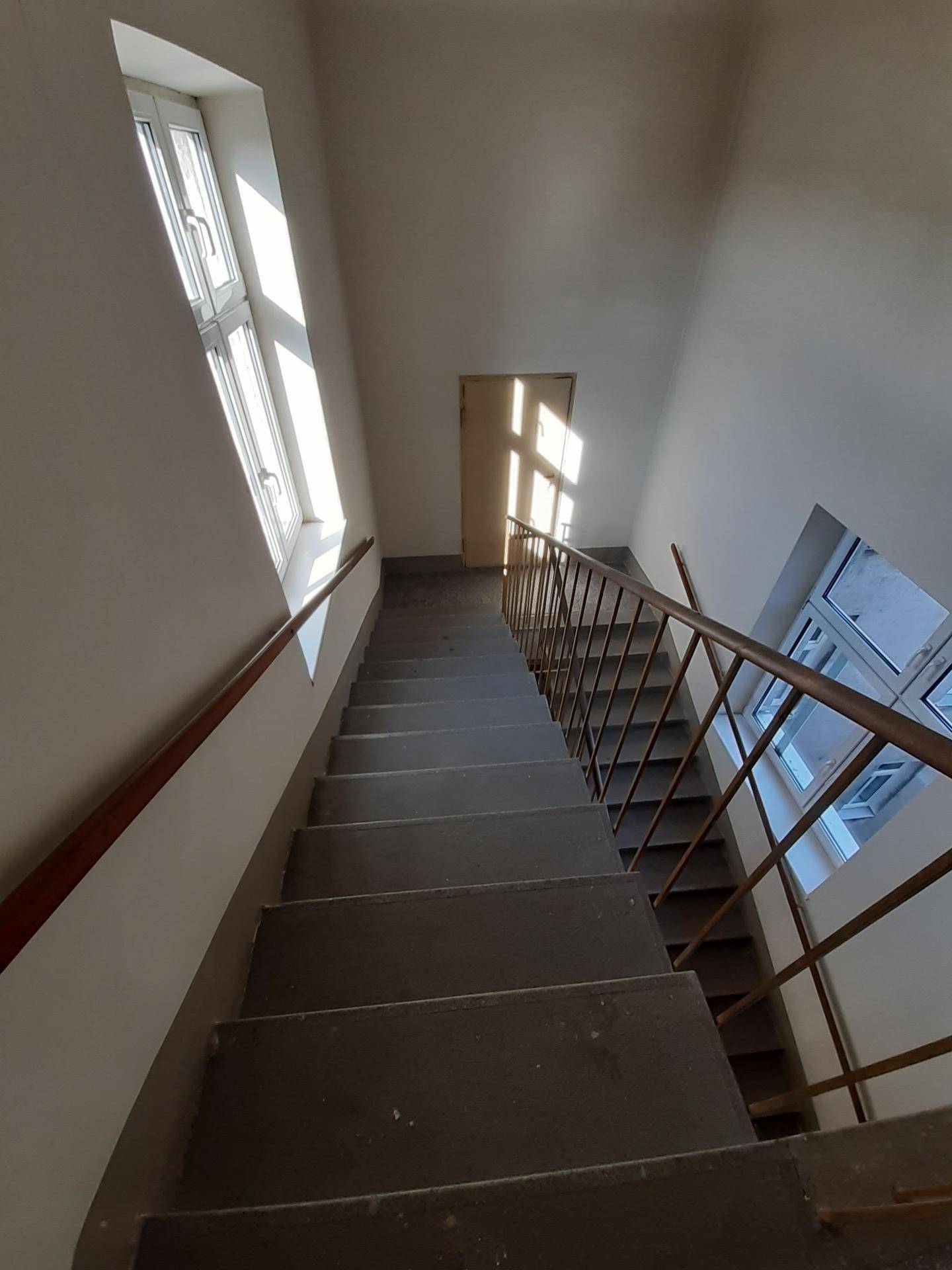 Heller Treppenaufgang mit natürlichem Lichteinfall durch große Fenster und einfacher Metallgeländer.