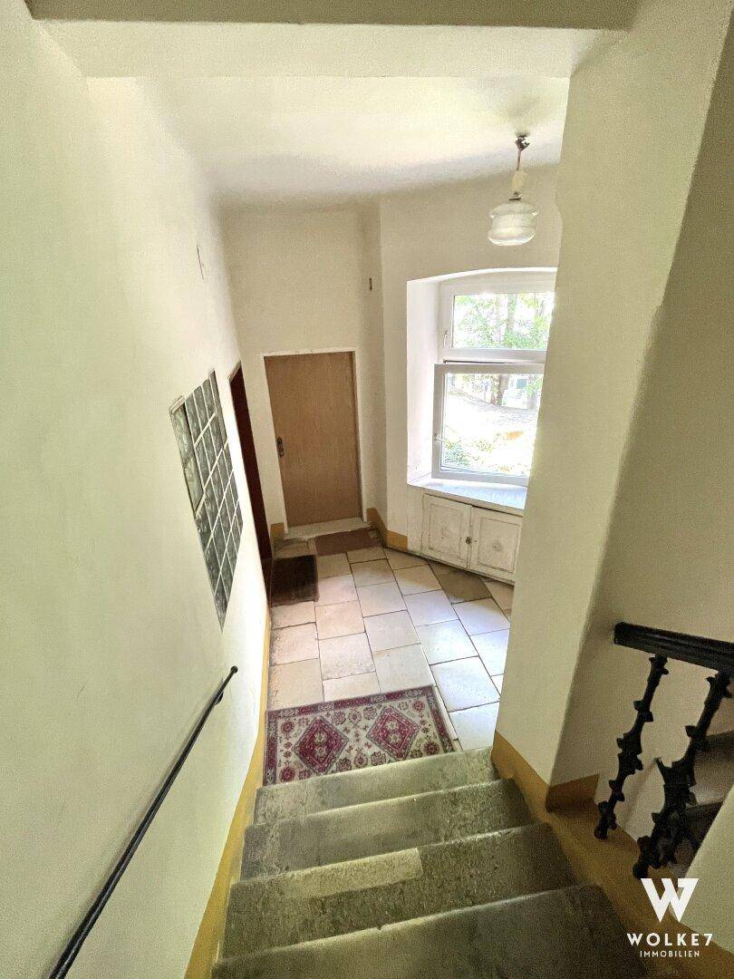 Treppenhaus mit gefliestem Boden, einem Fenster und traditionellem Geländer in einem Altbau.