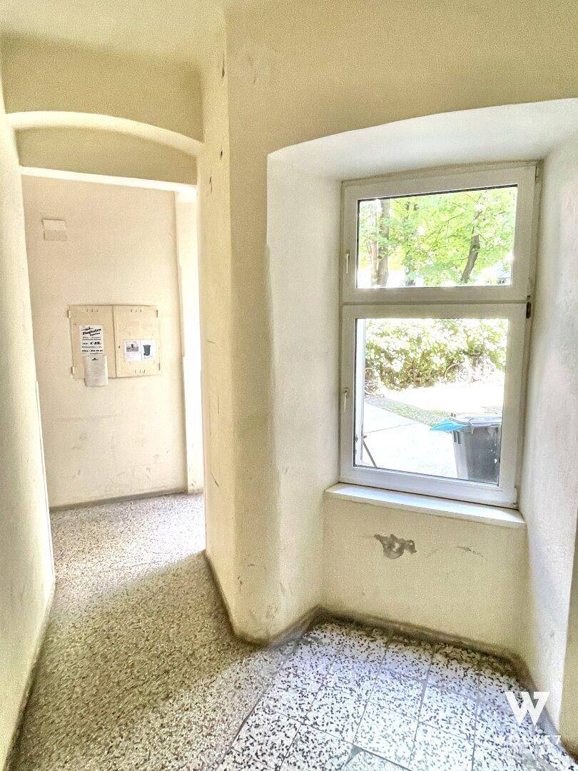 Heller Flurbereich mit Terrazzoboden und einem Fenster, das Tageslicht hereinlässt.