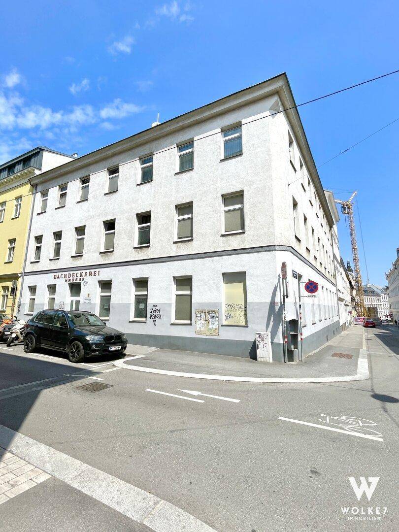 Ansicht des Eckgebäudes von der Straße, zeigt die Fassade mit Fenstern und einen sonnigen Tag.
