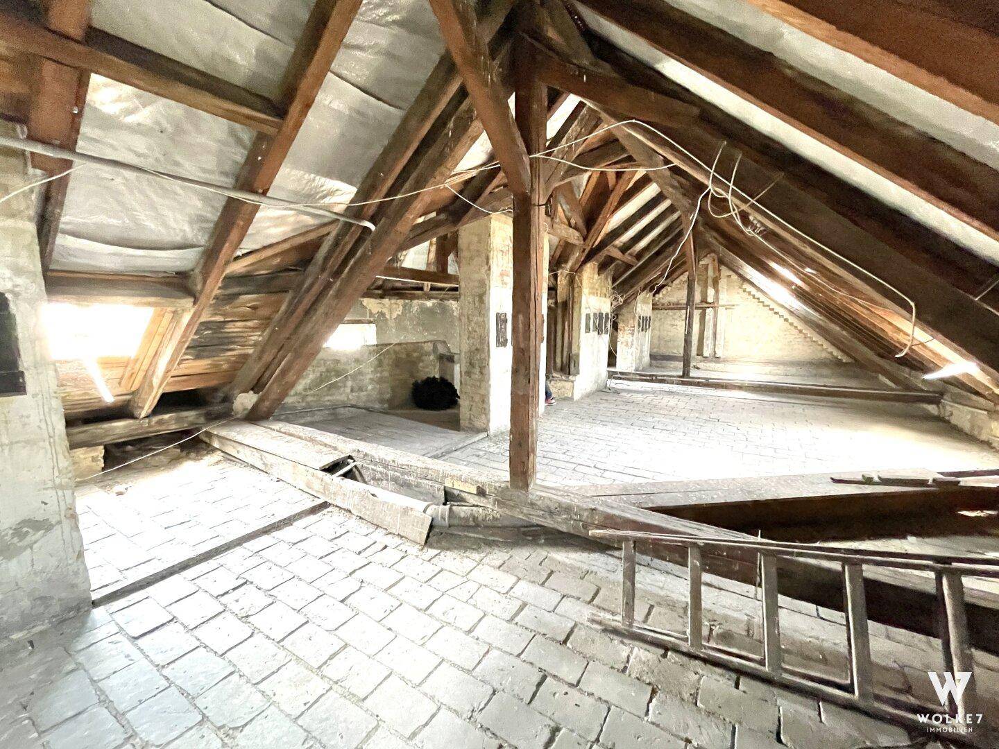 Geräumiger Dachboden mit sichtbaren Holzbalken und Ziegelboden, bereit für den Ausbau.