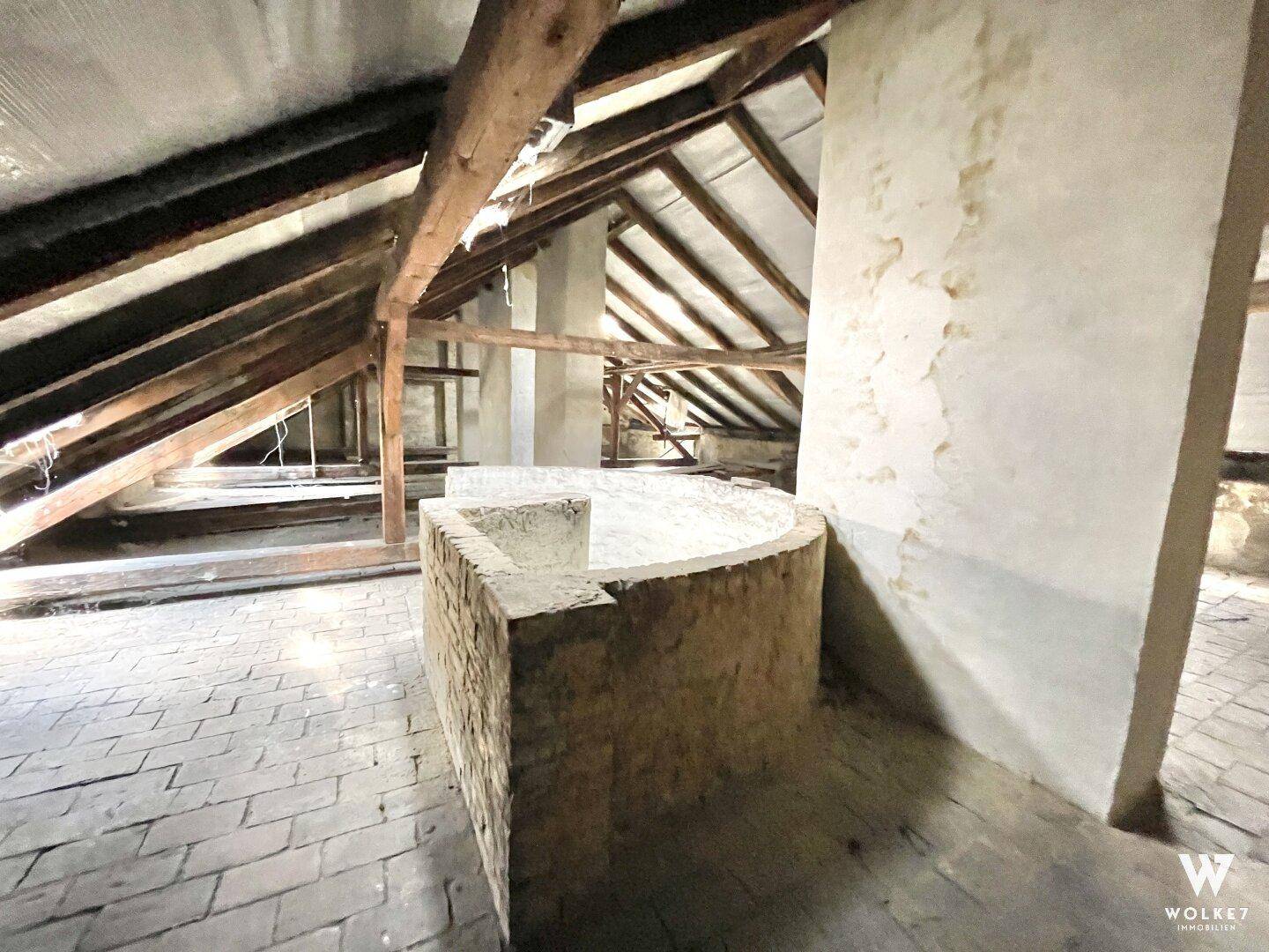 Großer Dachboden mit sichtbaren Holzbalken und einem gemauerten Element, ideal für Ausbau.