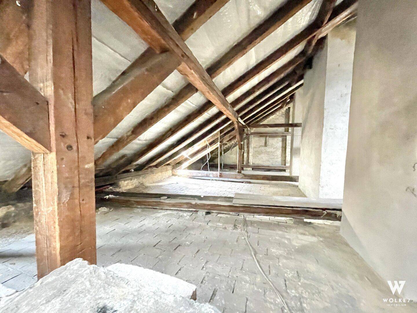 Heller Dachboden mit freiliegenden Holzbalken und Ziegelboden, bereit für Renovierung.
