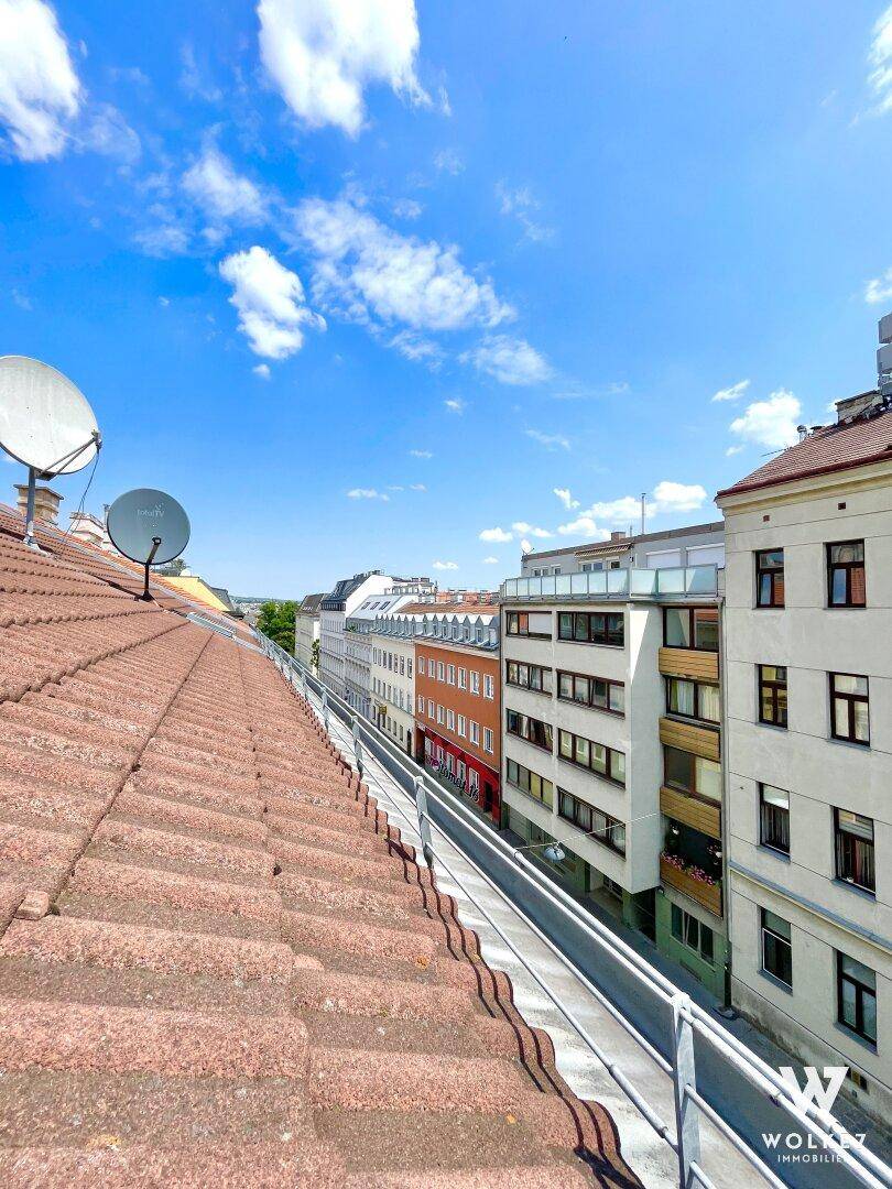 Blick über die Dächer einer Stadt mit roten Ziegeln und Satellitenschüsseln unter blauem Himmel.