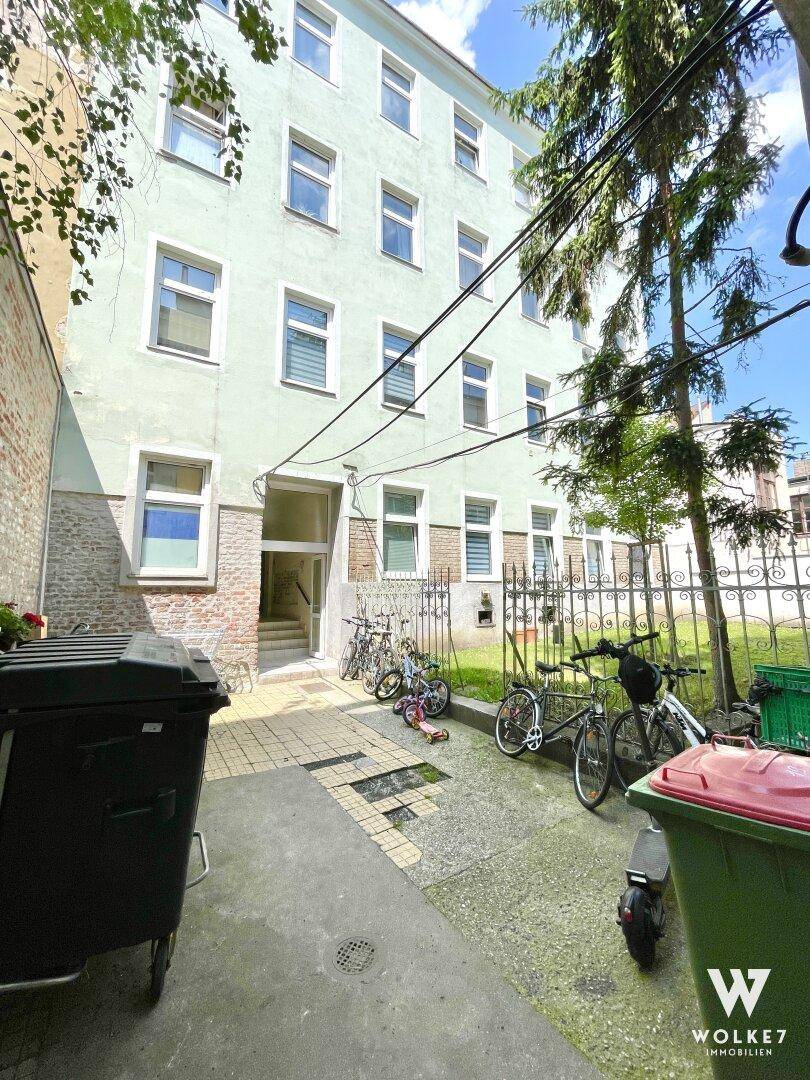 Hinterhof eines Mehrfamilienhauses mit gepflastertem Bereich, Fahrrädern und Mülltonnen.