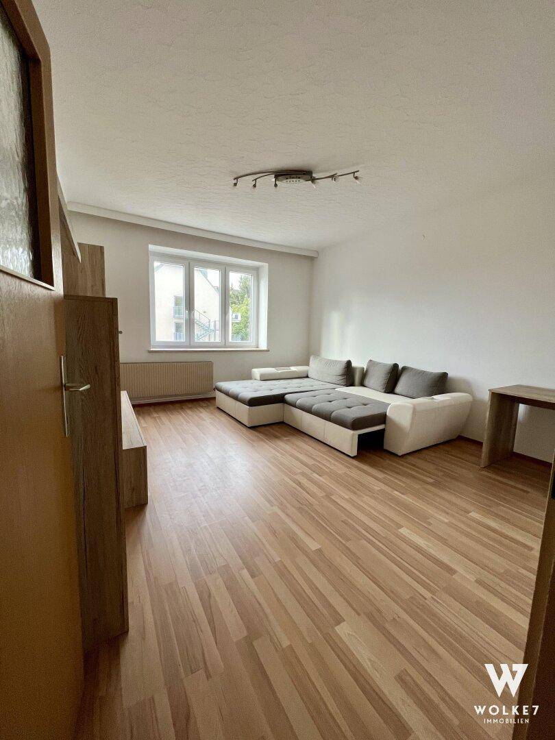 Geräumiges Wohnzimmer mit ausziehbarem Sofa und Laminatboden, bereit zur individuellen Gestaltung.