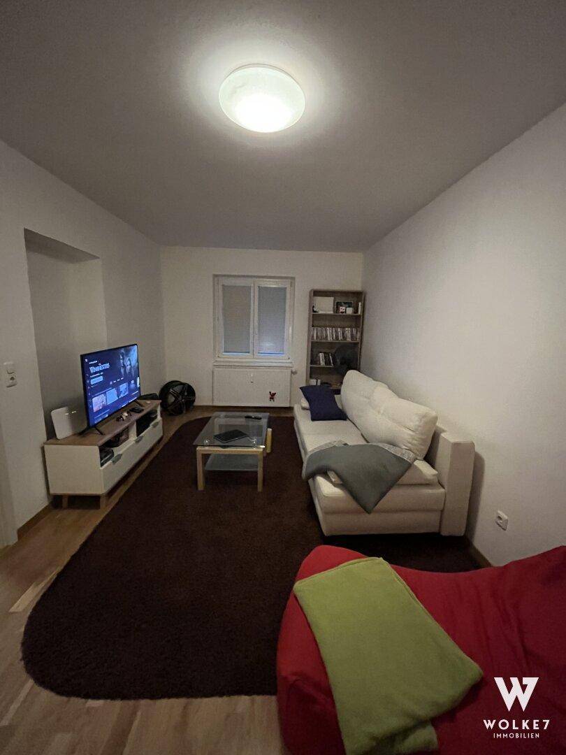 Gemütliches Wohnzimmer mit Sofa, Fernseher, Bücherregal und Holzboden.