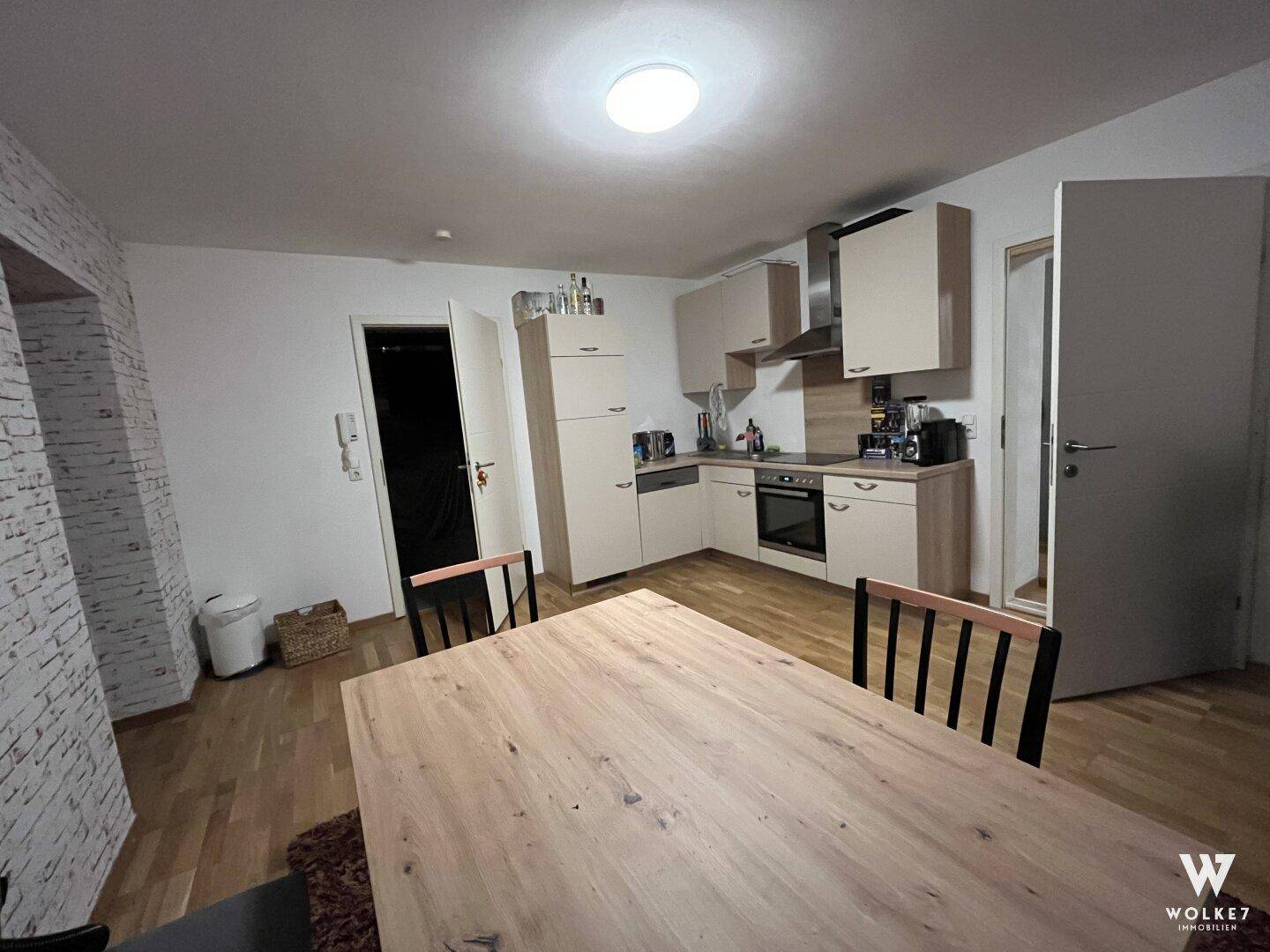 Helle Küche mit beigen Schränken, Holzboden und Essbereich in modernem Design.