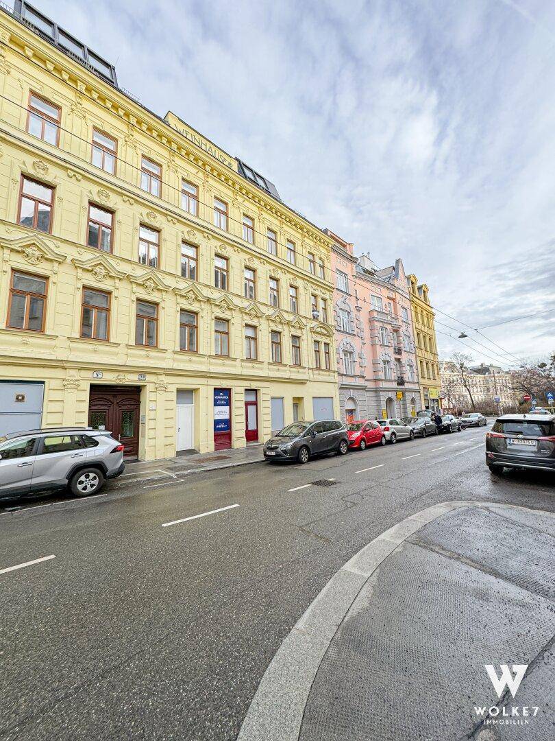 Historisches Gebäude mit gelber Fassade an einer belebten Straße mit parkenden Autos.