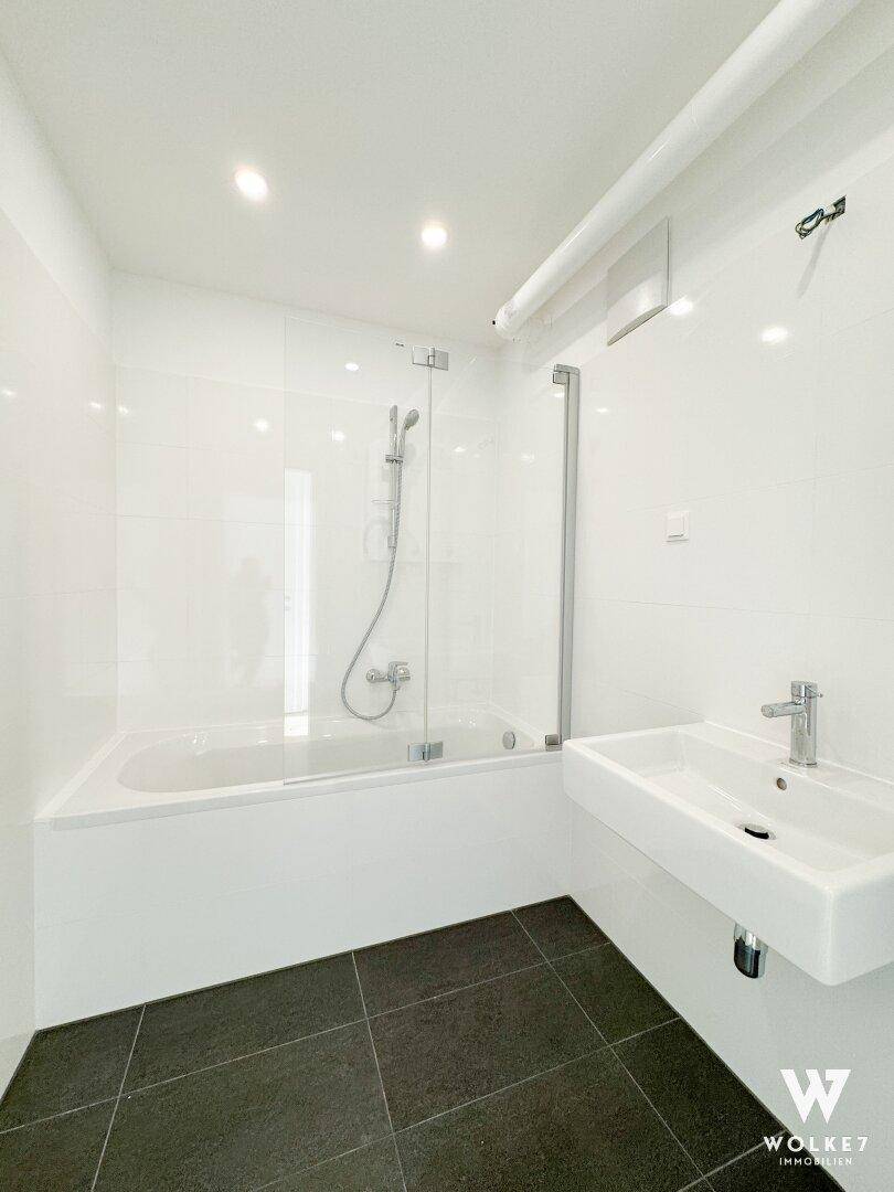 Modernes Badezimmer mit Badewanne, Glasduschwand und Einzelwaschbecken auf dunklen Fliesen.