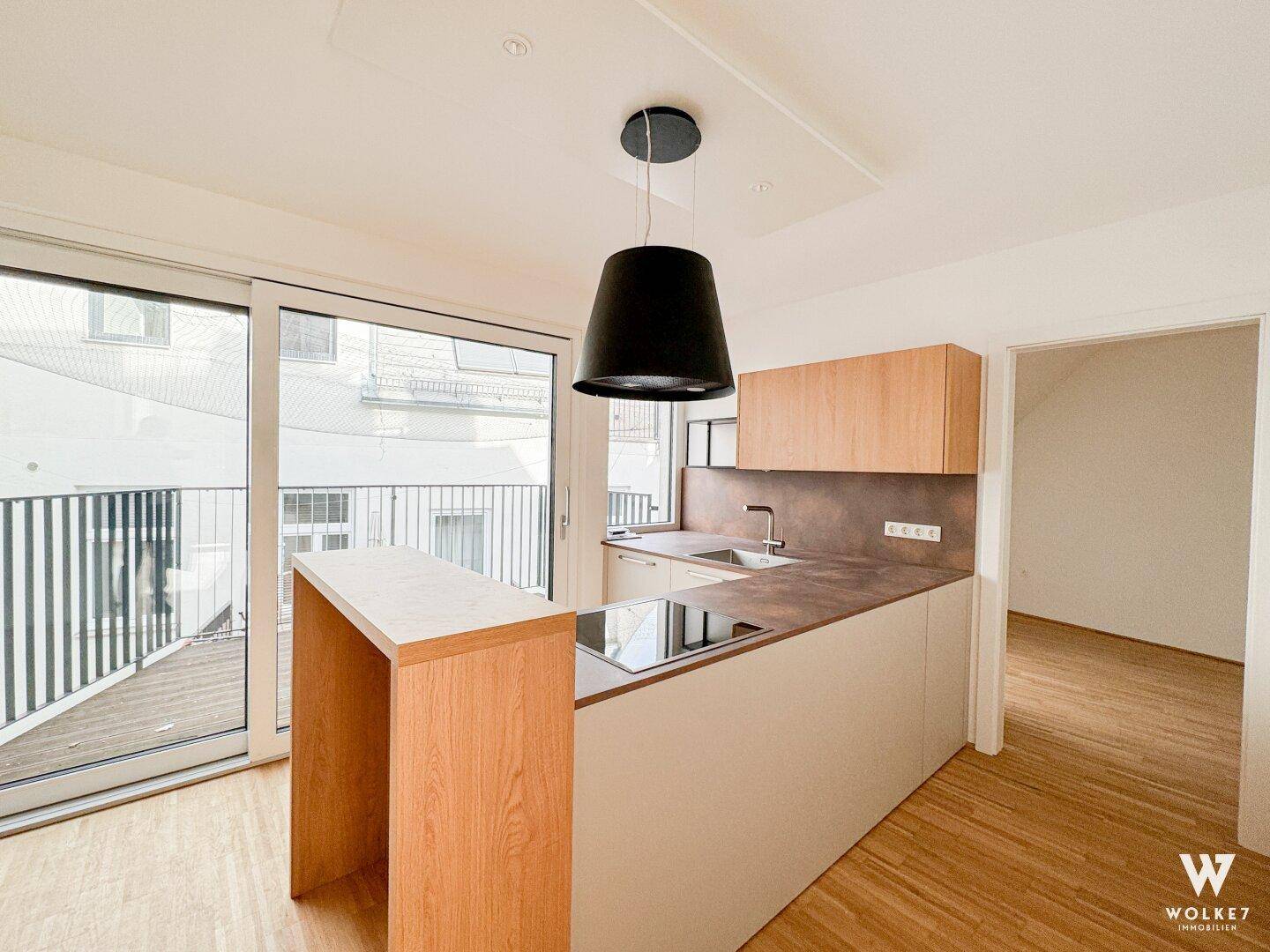 Moderne Küche mit Holzelementen, Kücheninsel mit Kochfeld und Zugang zu einem Balkon.