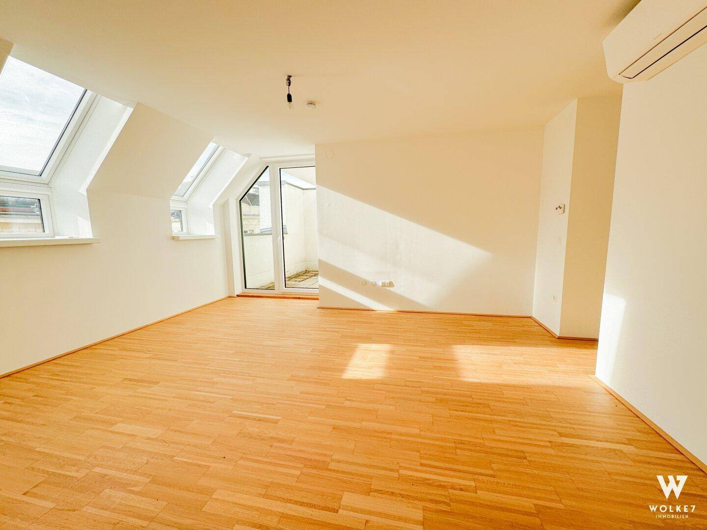 Geräumiges, leeres Wohnzimmer mit Holzboden, Dachfenstern und viel natürlichem Licht.
