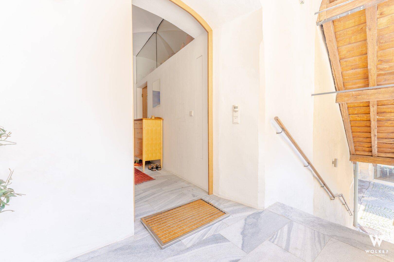 Eingangsbereich mit Steinfliesen, Holztreppe und einem Garderobenschrank im Hintergrund.