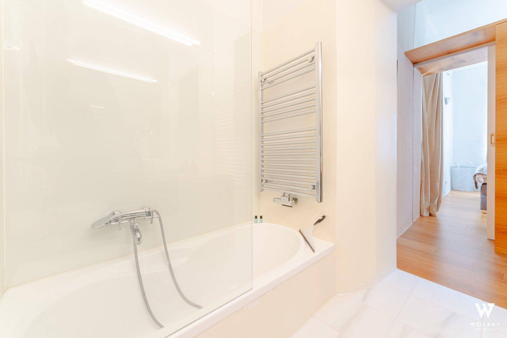 Helles Badezimmer mit Badewanne, Duschabtrennung und beheiztem Handtuchhalter.