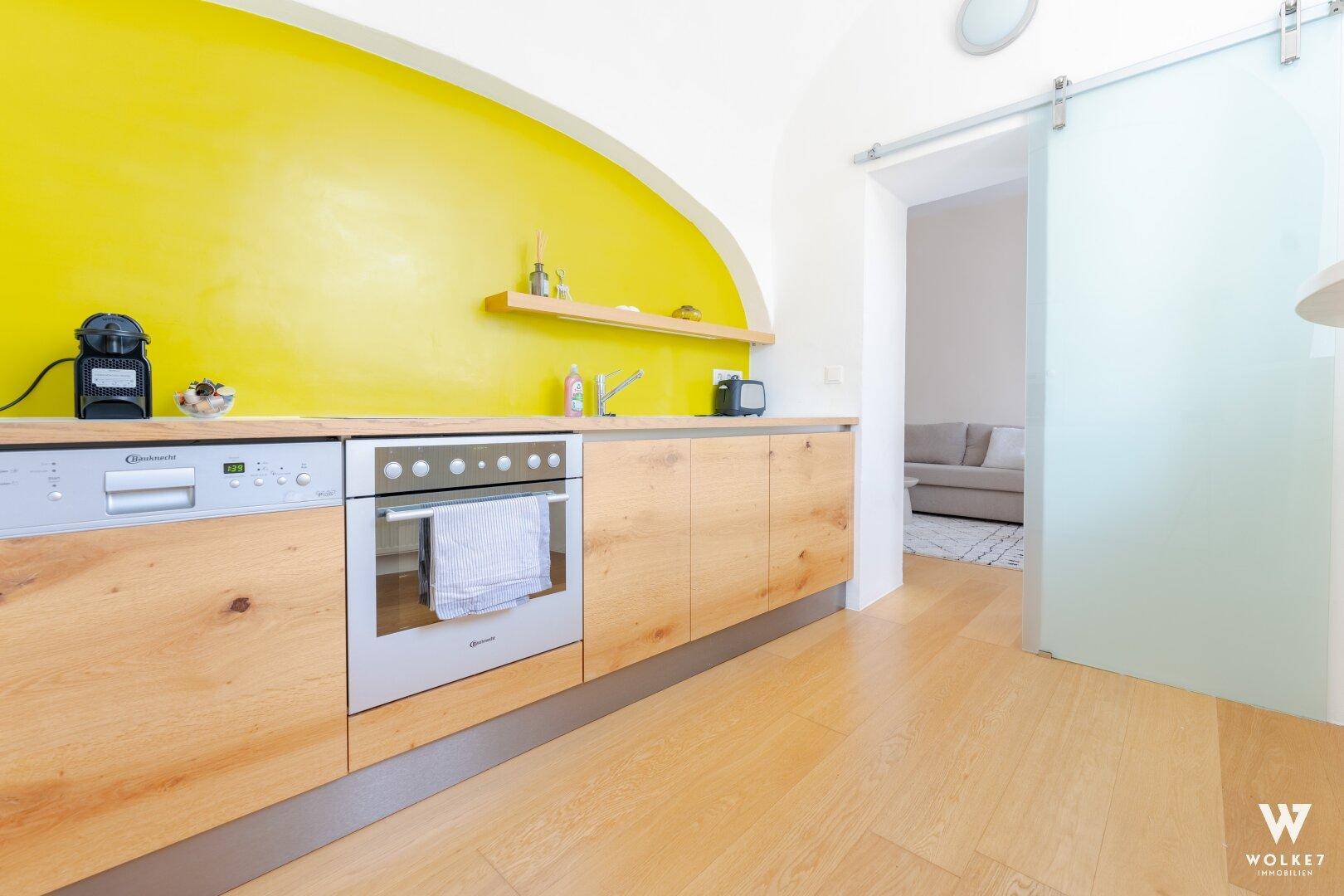 Moderne Küche mit gelber Akzentwand, Holzelementen und integrierten Geräten.