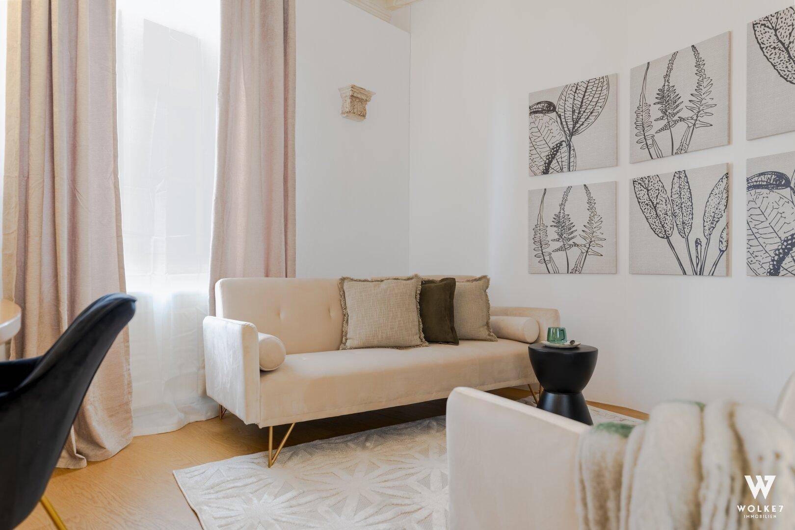 Gemütliches Wohnzimmer mit beigem Sofa, Holzboden und dekorativen Wandbildern in hellem Ambiente.