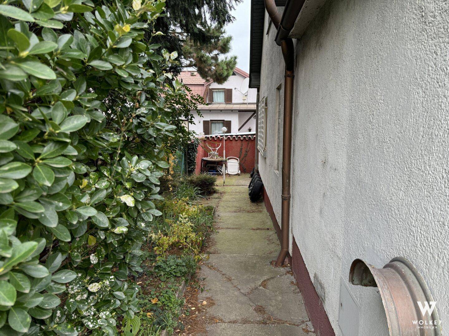 Schmaler Gartenweg entlang des Hauses, der zu einem hinteren Bereich führt.