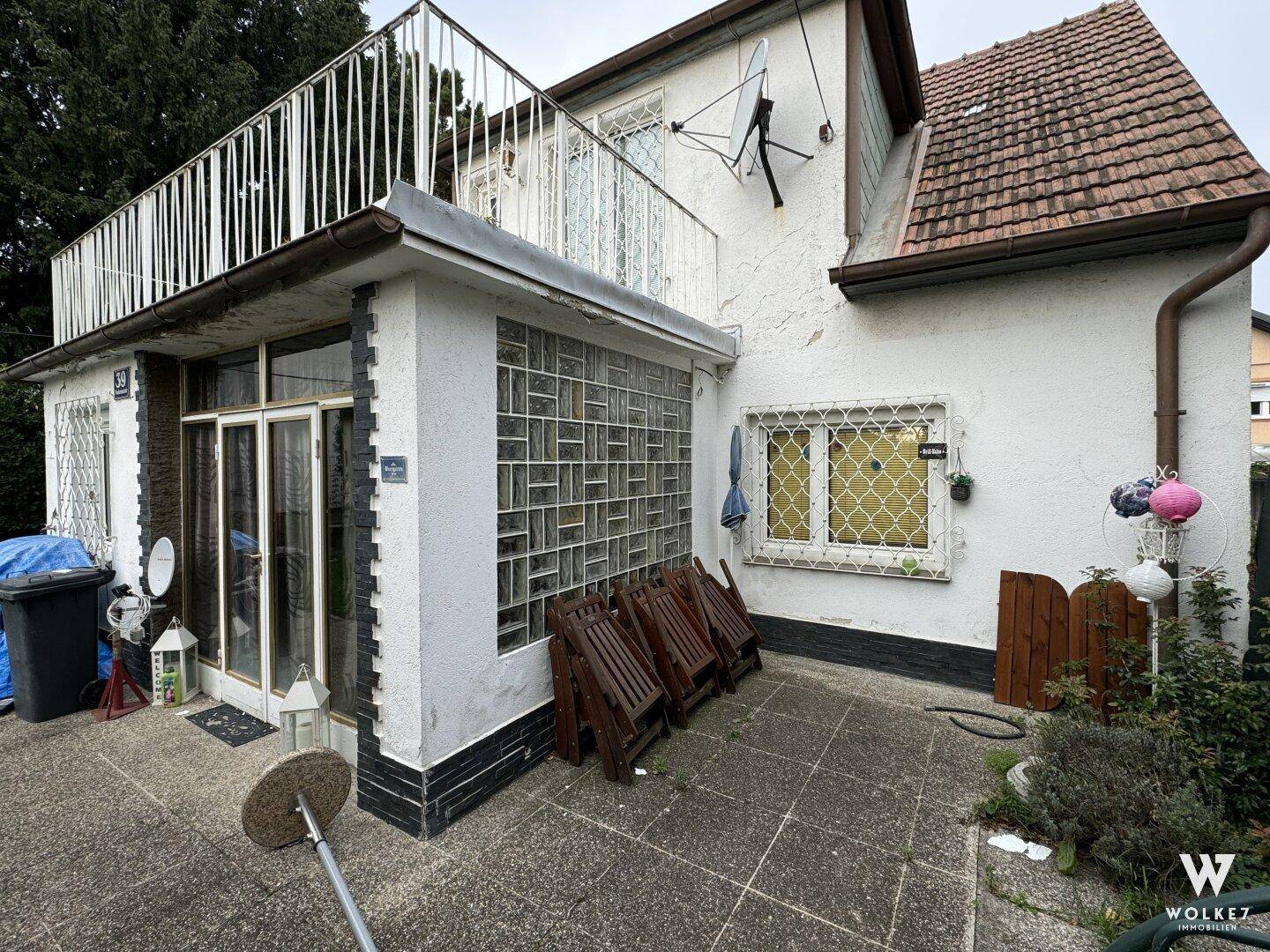 Seitlicher Blick auf das Haus mit einer gepflasterten Terrasse und einem Balkon im Obergeschoss.