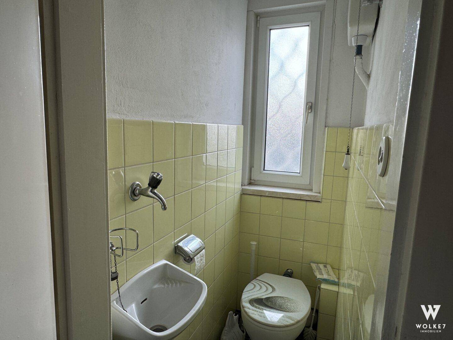 Kleines Gäste-WC mit gelben Fliesen, Waschbecken und einem schmalen Fenster.