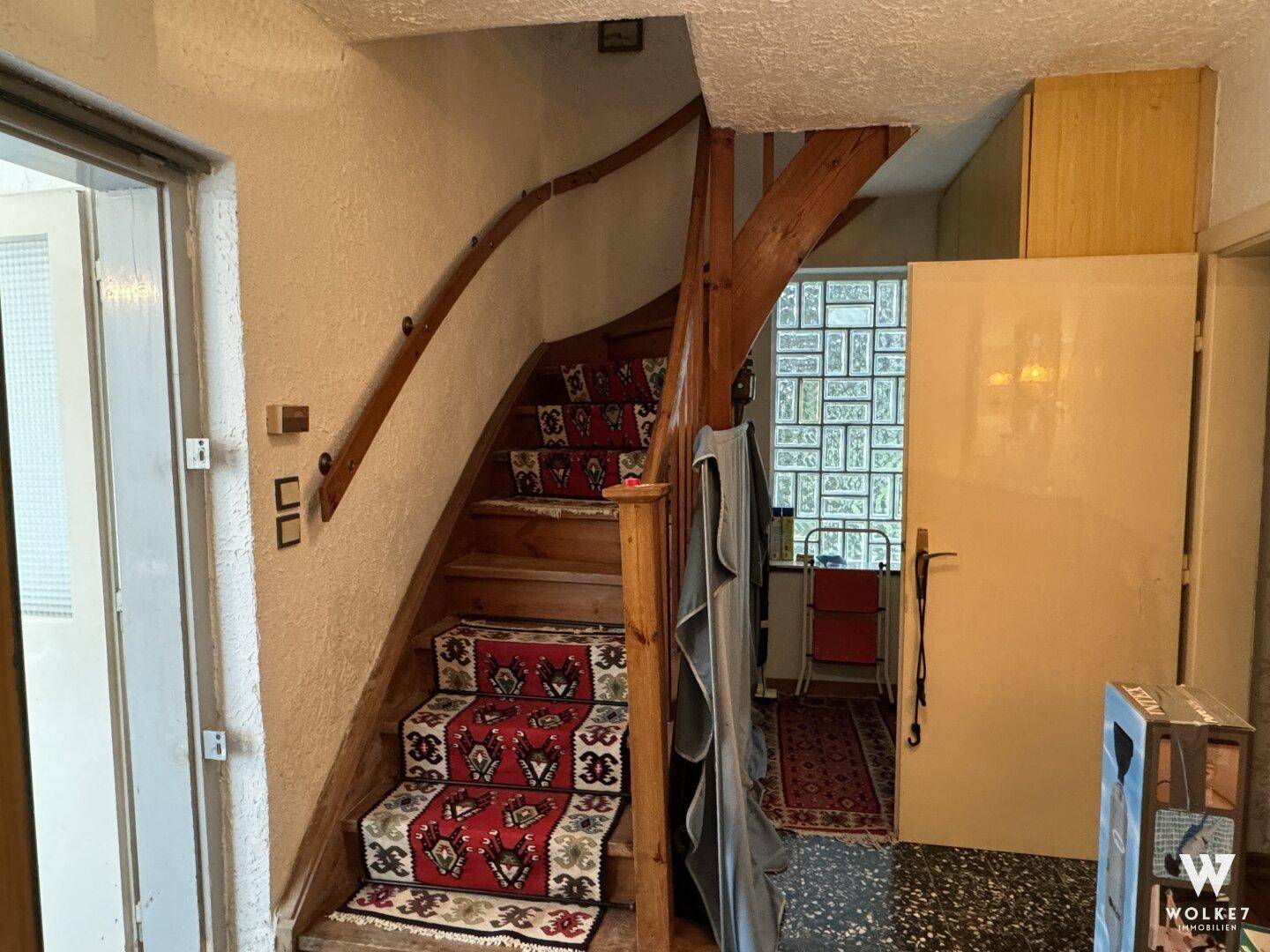 Flur mit einer Holztreppe, die mit einem gemusterten Teppichläufer belegt ist.