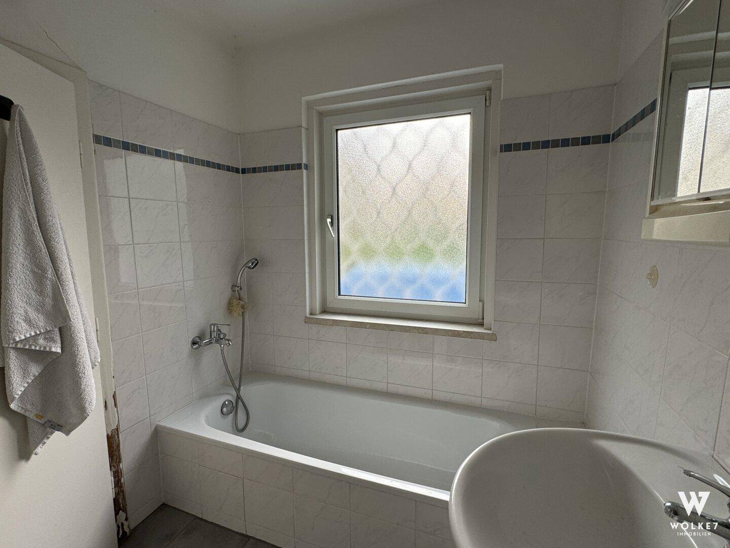 Badezimmer mit Badewanne, Waschbecken und einem Fenster für Tageslicht.