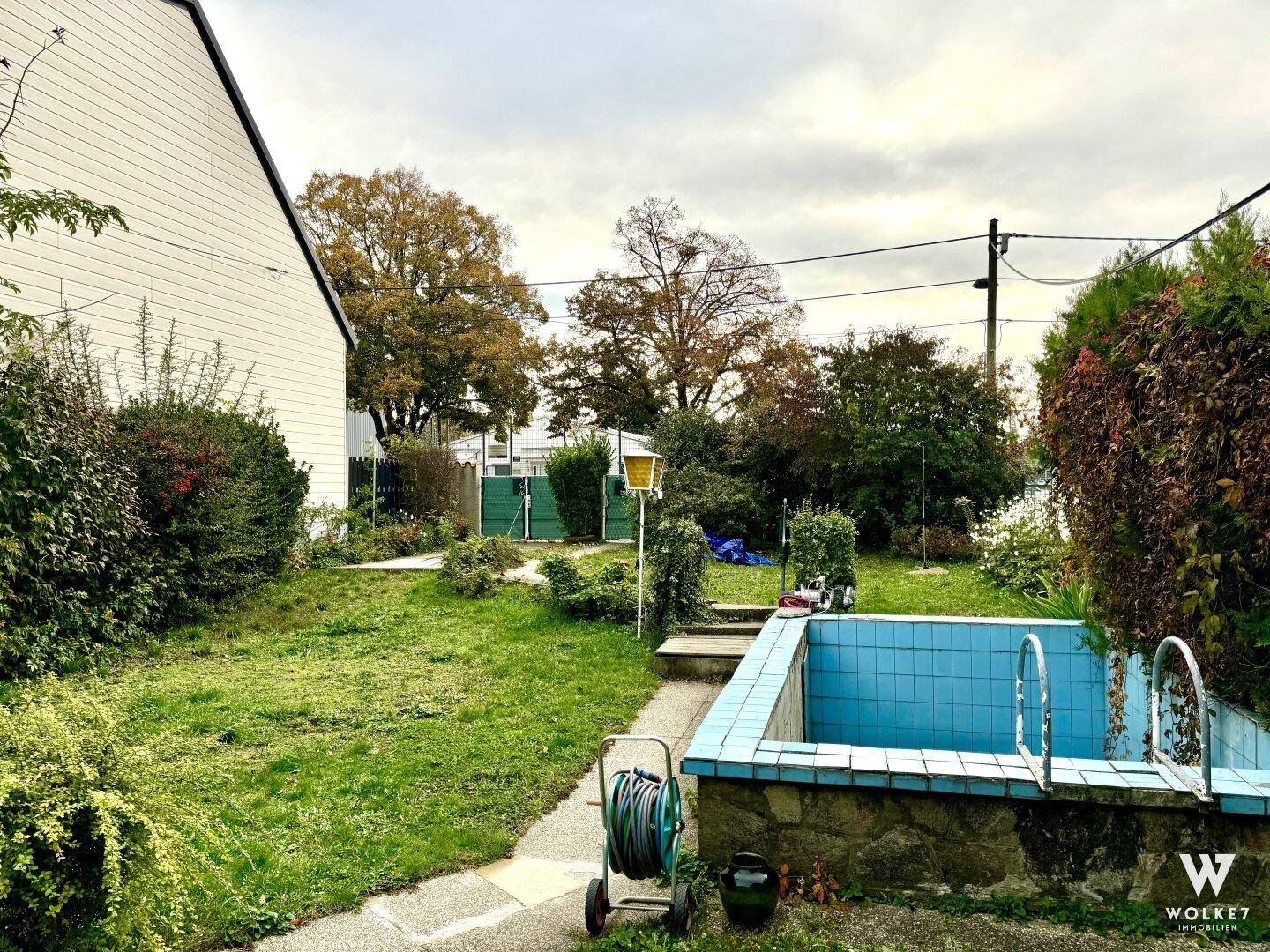 Weitläufiger Gartenbereich mit Rasenfläche, einem kleinen Becken und umgebenden Bäumen.