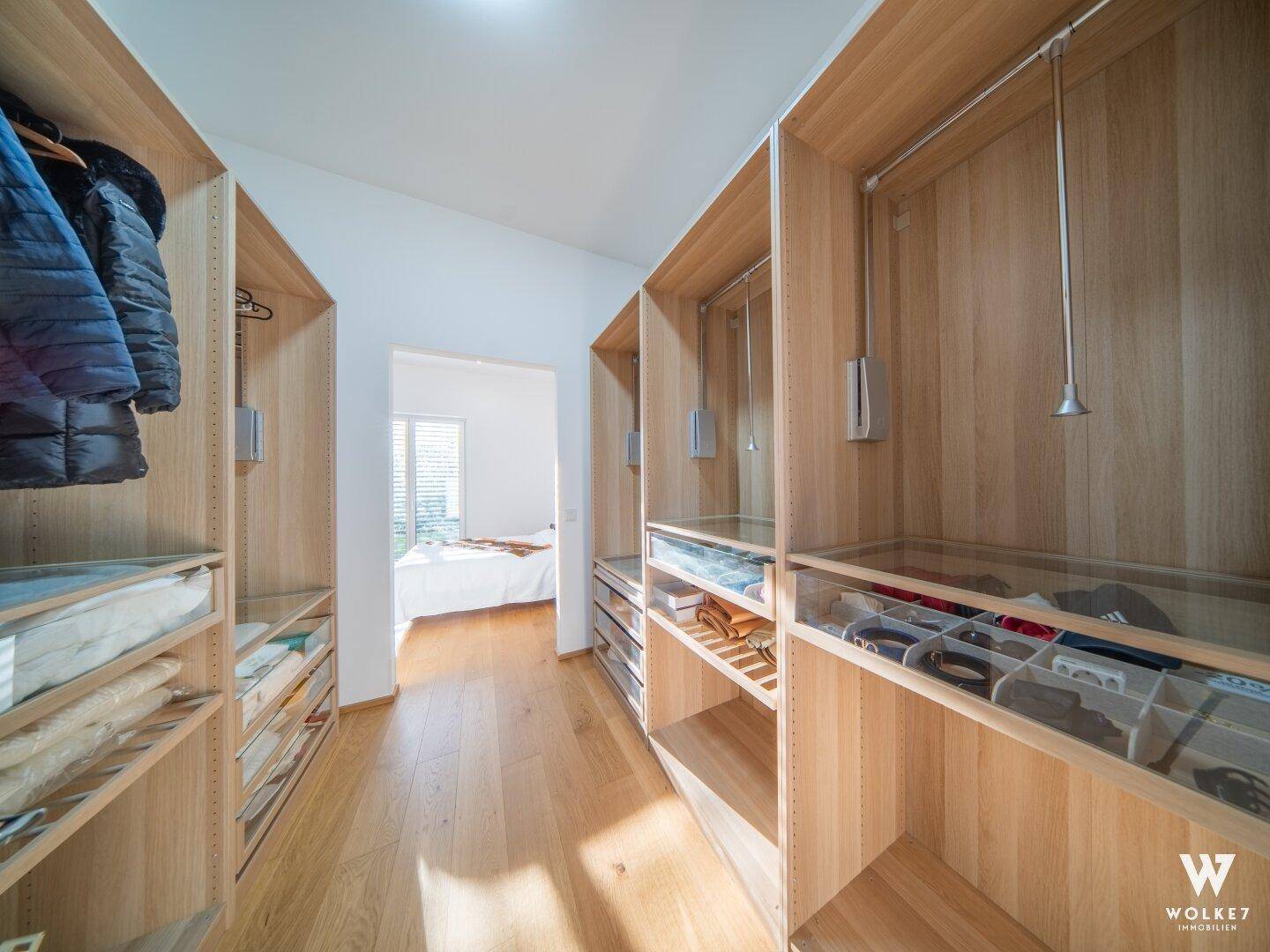Geräumiger begehbarer Kleiderschrank mit Holzregalen und viel Stauraum, angrenzend an ein Schlafzimmer.